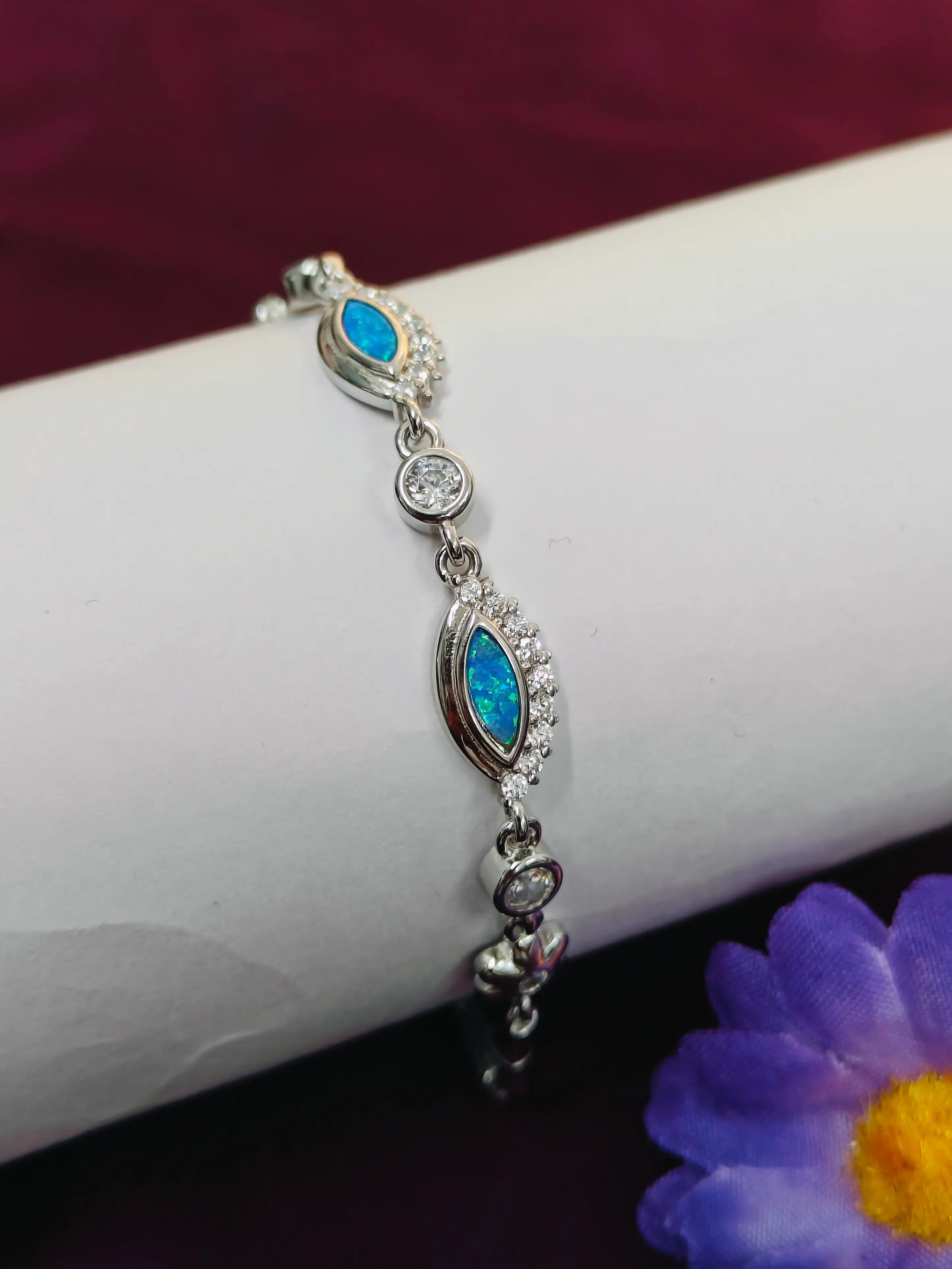 Silver bracelet with blue stones on a white arm, purple flower in the corner