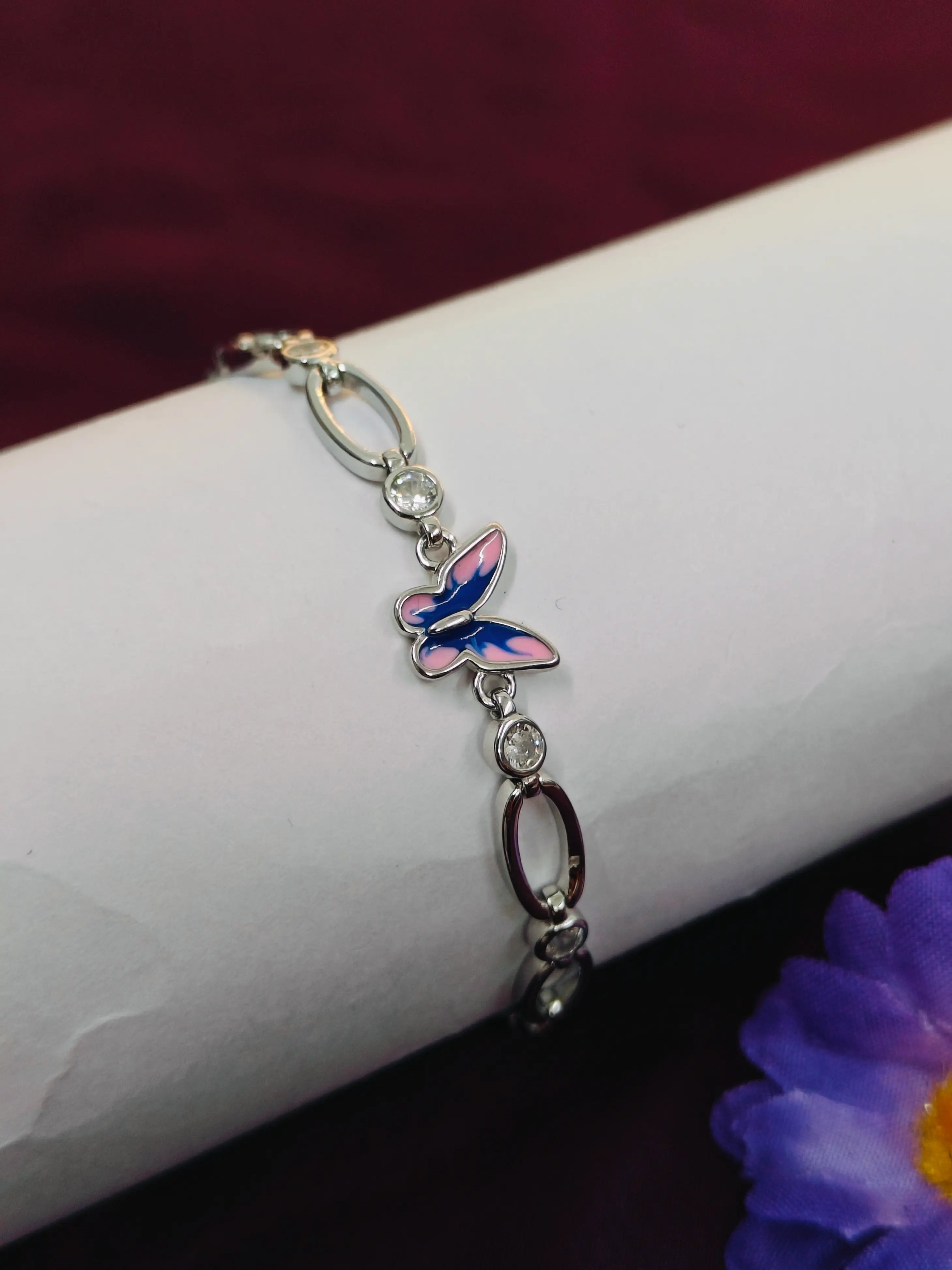 Butterfly charm bracelet on a wrist with a purple flower in the background