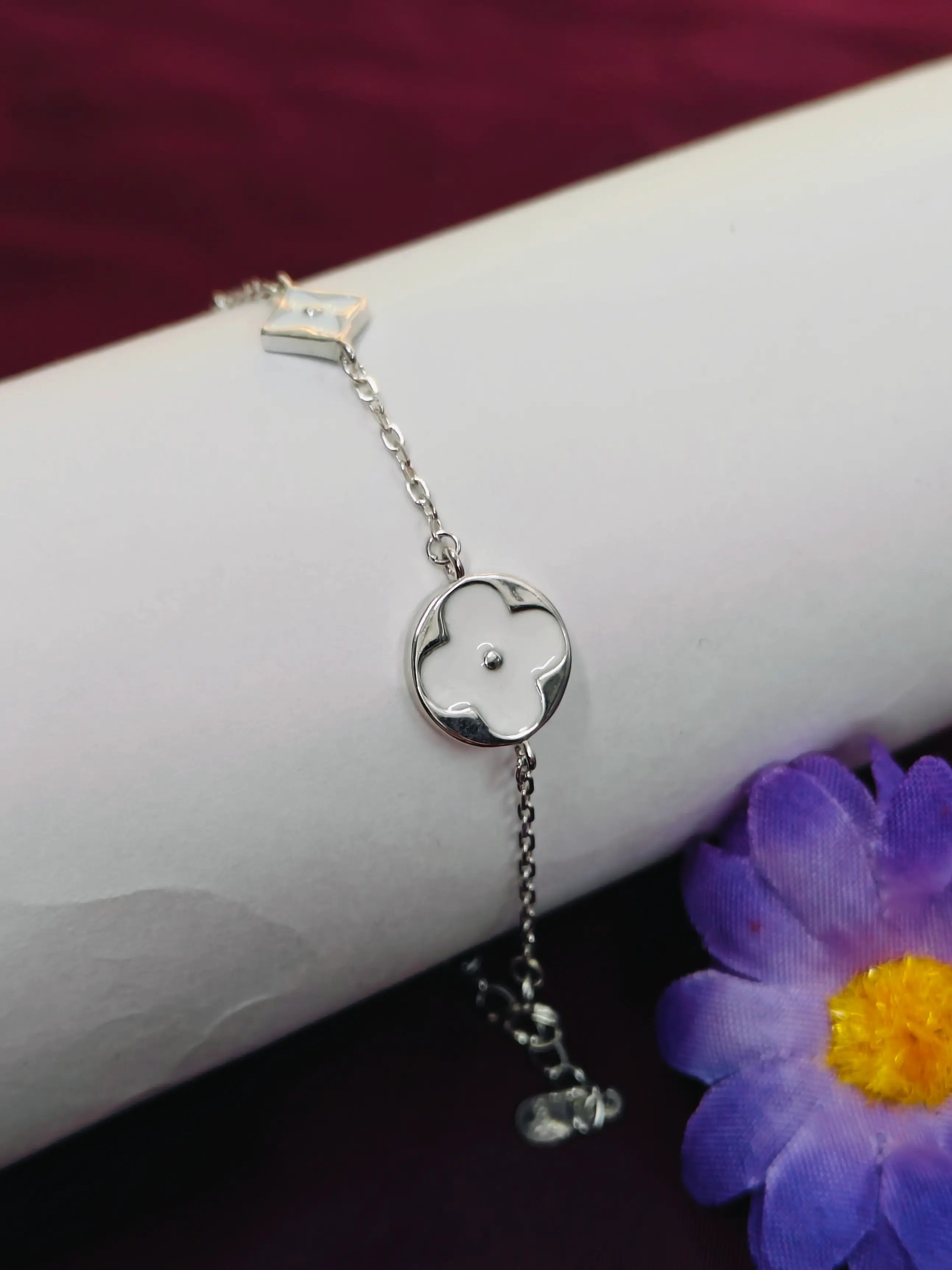 Silver bracelet with a clover-shaped charm on a wrist, next to a purple flower.