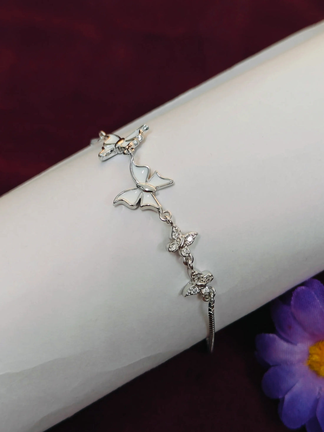 Silver bracelet with butterfly designs on a white surface with a purple flower in the background