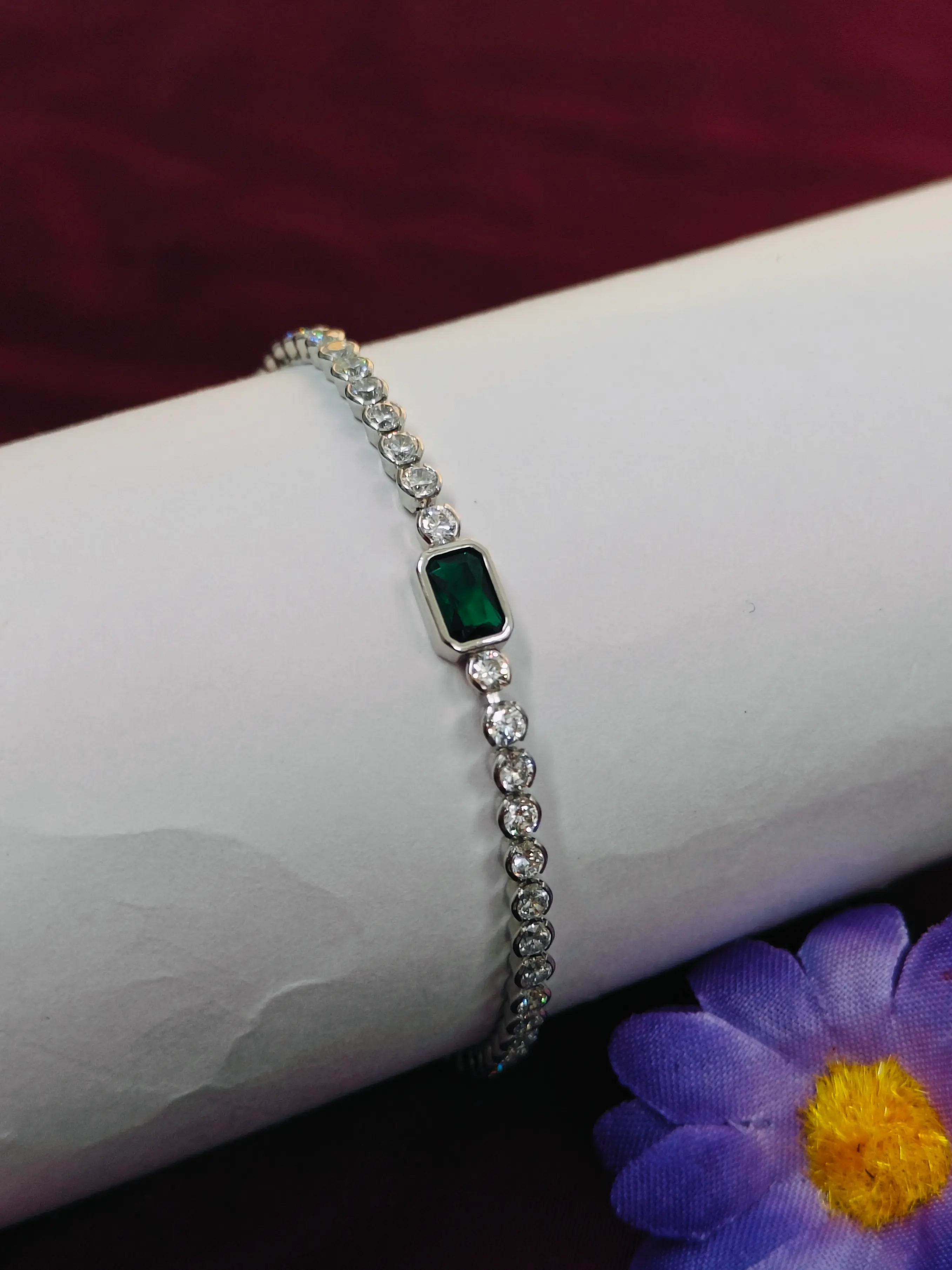 Silver bracelet with a green gemstone on a wrist, with a purple flower in the background.