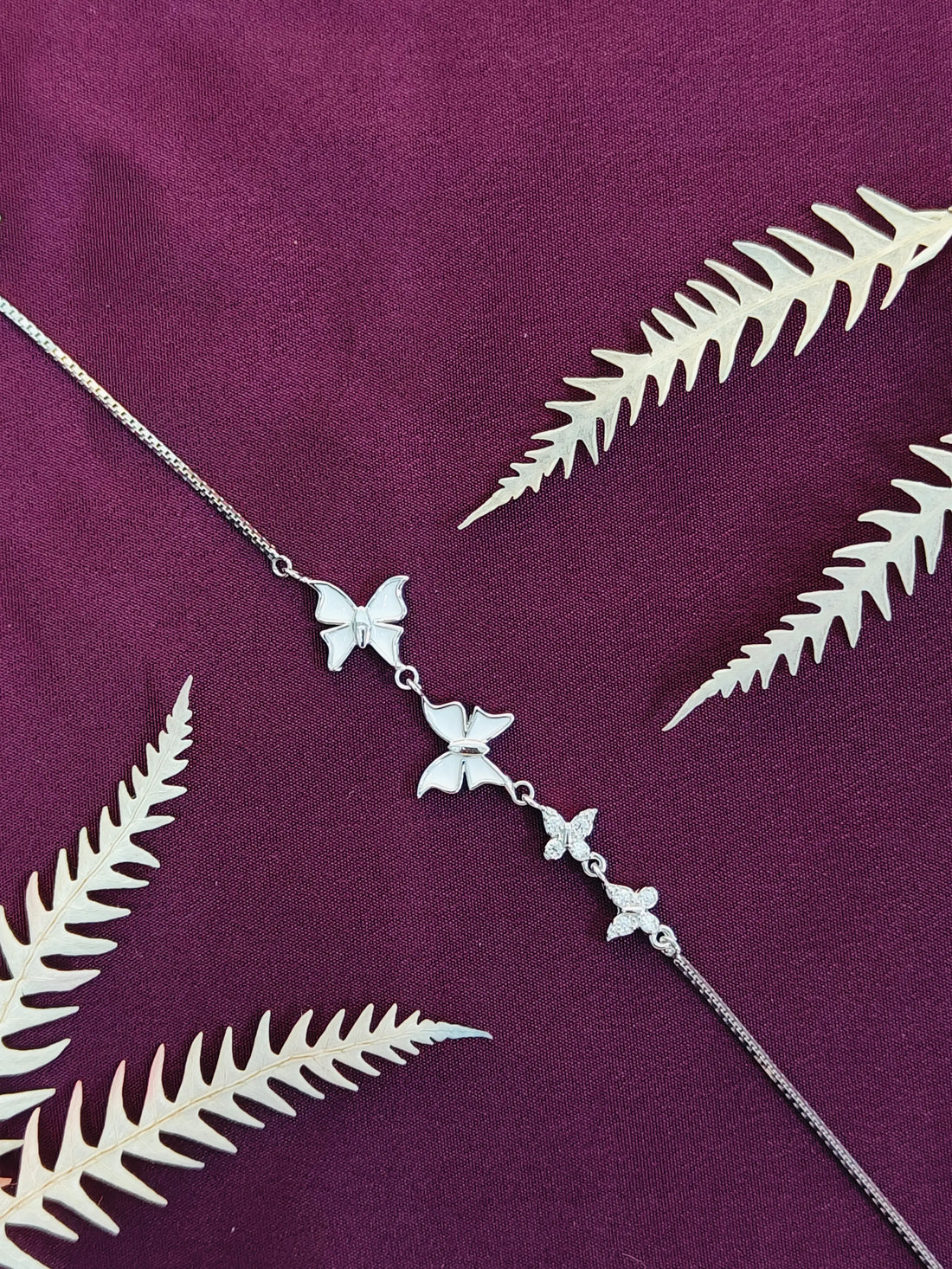 Silver necklace with butterfly and leaf designs on a purple fabric background