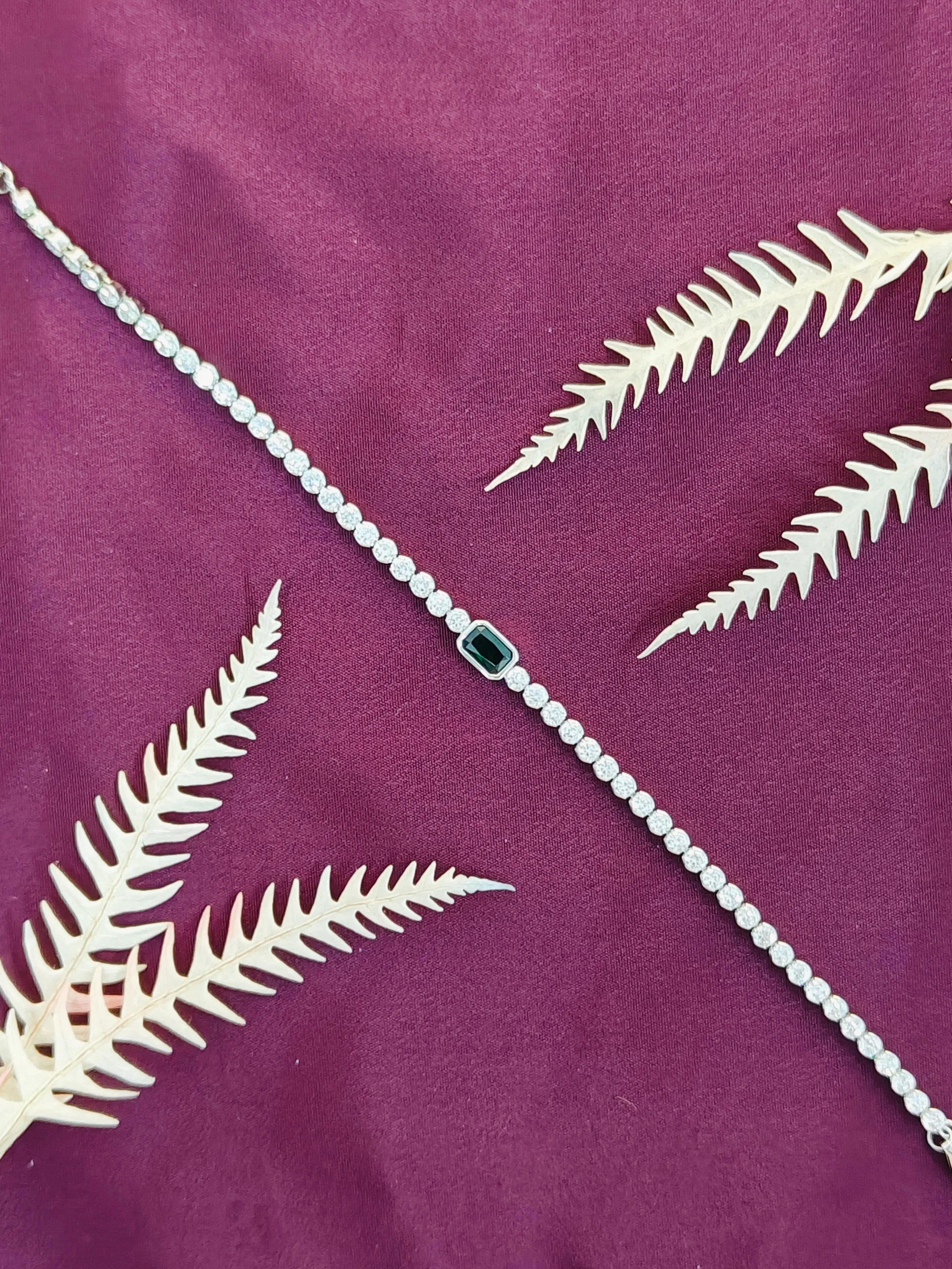 Silver necklace with a green gemstone on a purple fabric background