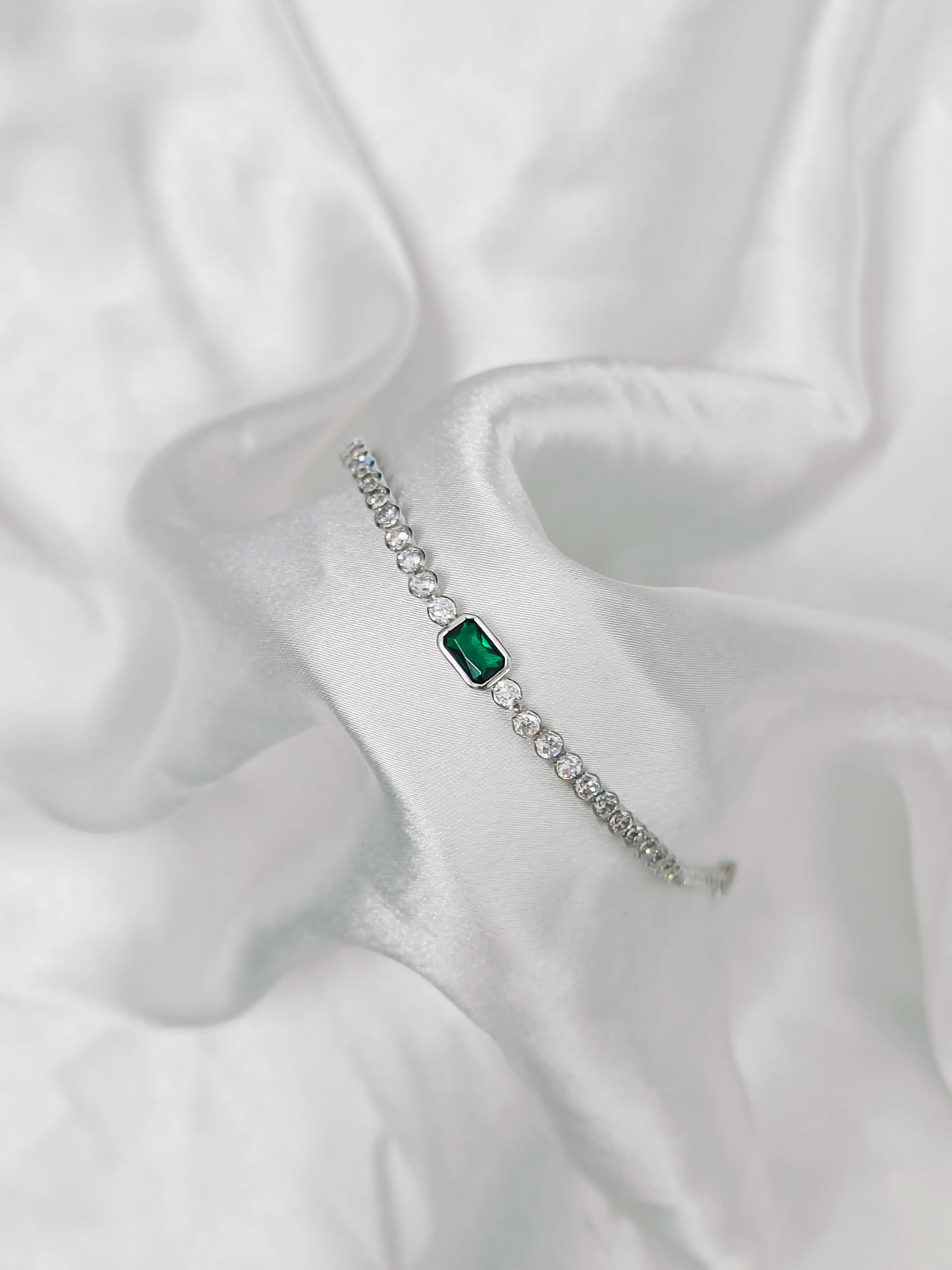 Silver bracelet with a green gemstone on a white fabric background