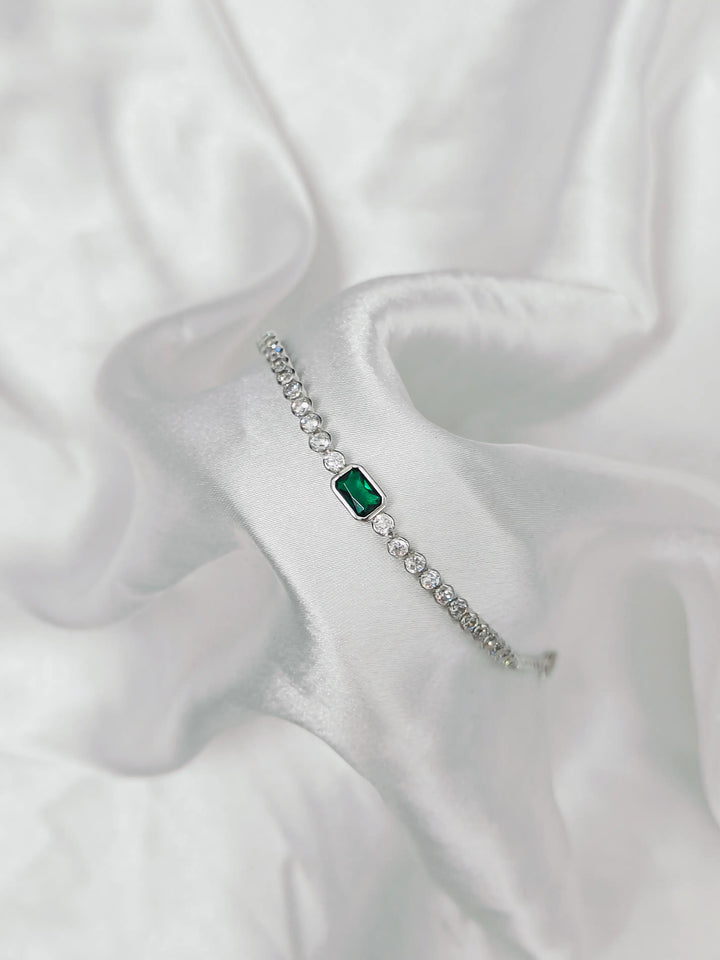 Silver bracelet with a green gemstone on a white fabric background