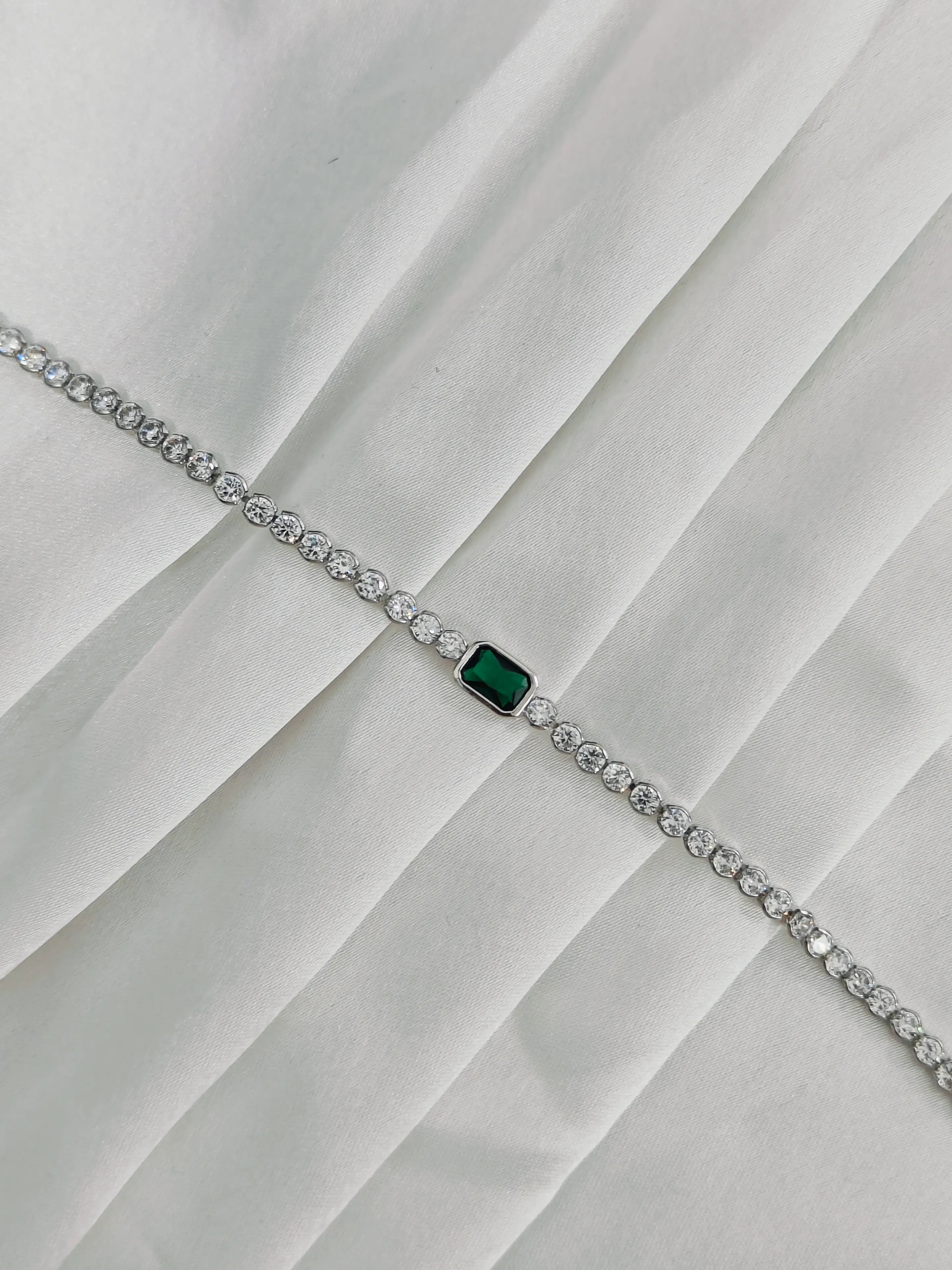 Silver bracelet with a green gemstone on a white fabric background