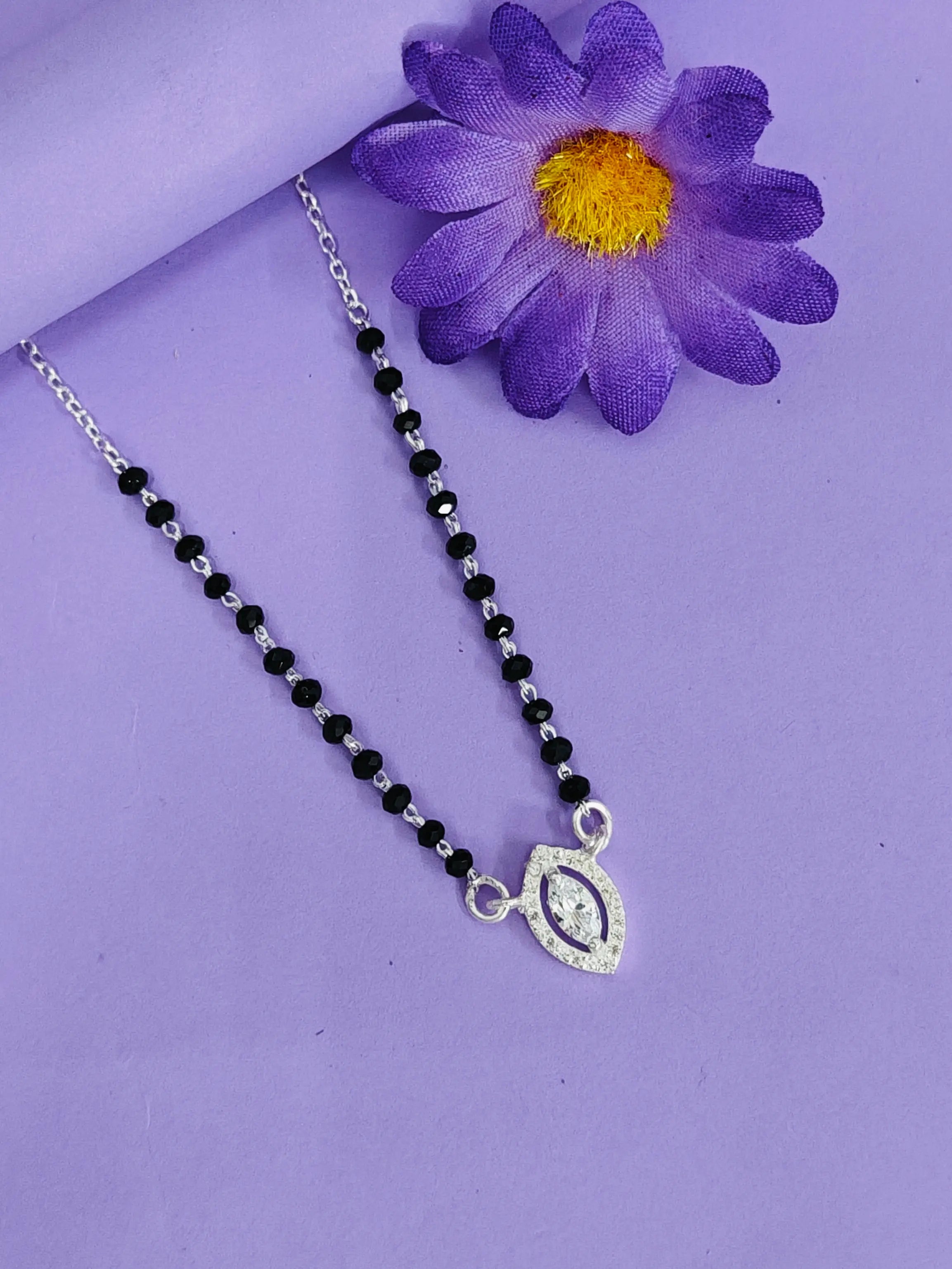 Necklace with black beads and a silver pendant on a purple background with a purple flower.