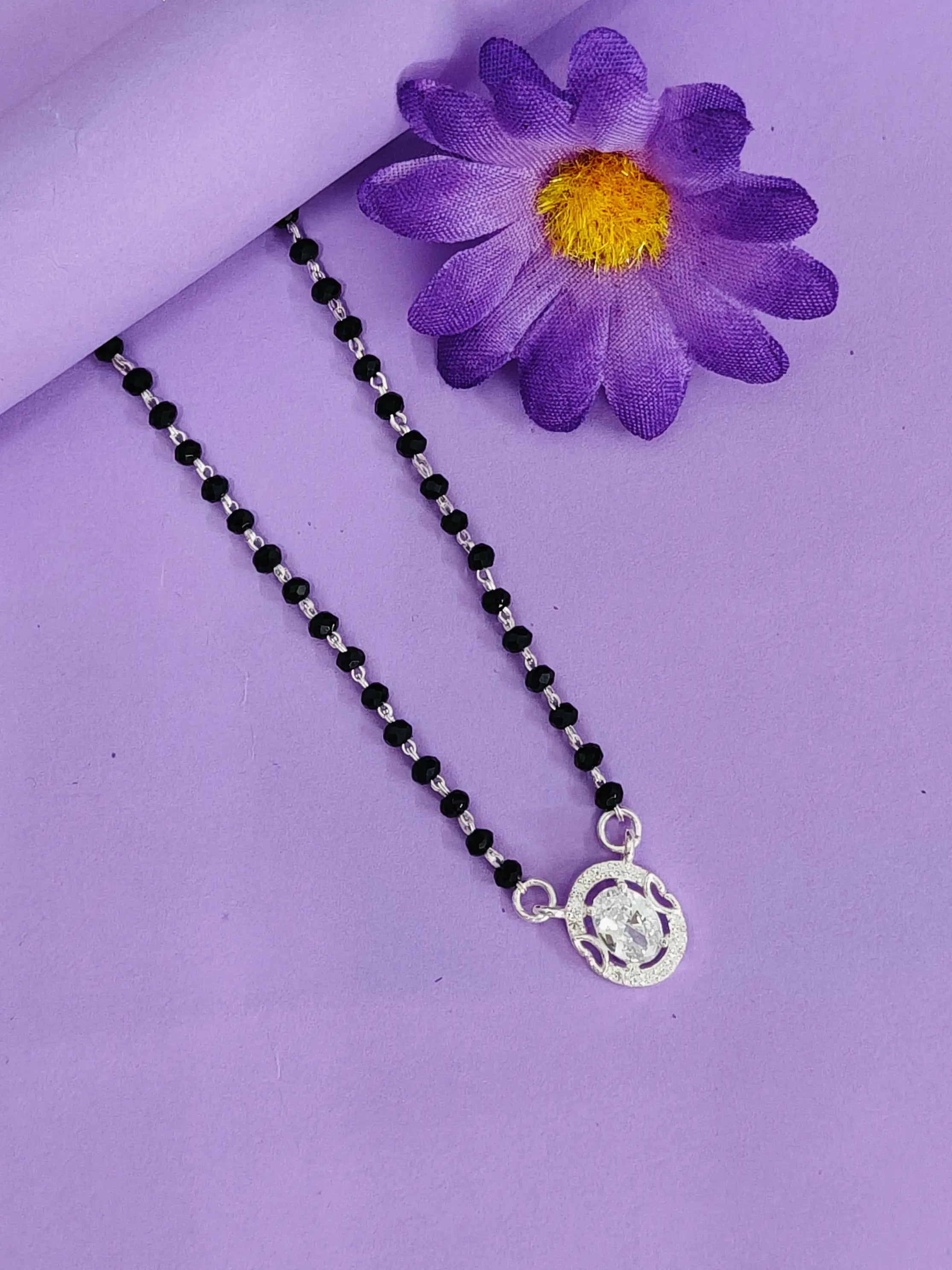 Necklace with black beads and a silver pendant on a purple background with a purple flower.