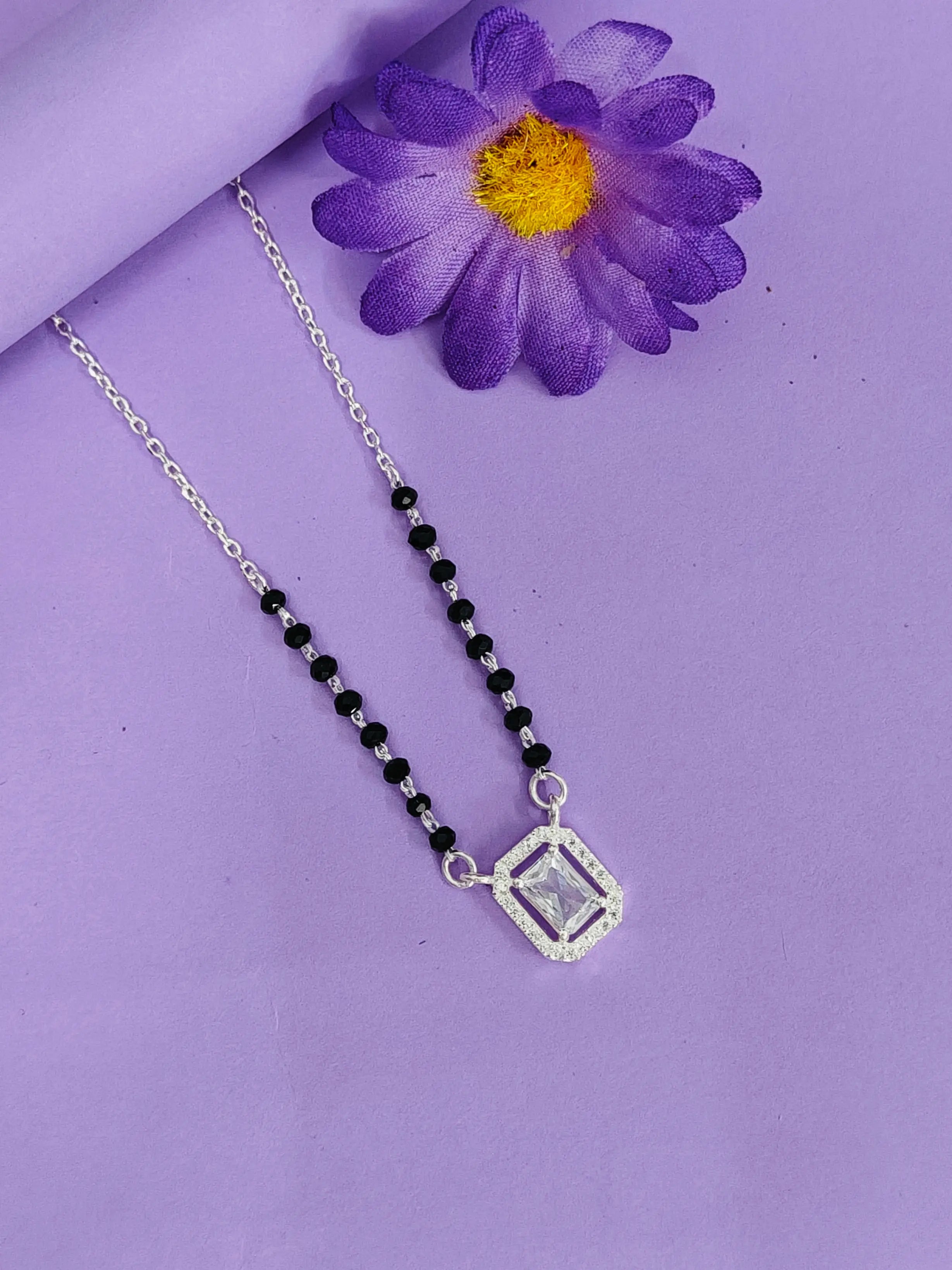 Necklace with a black beaded chain and silver pendant on a purple background with a purple flower.