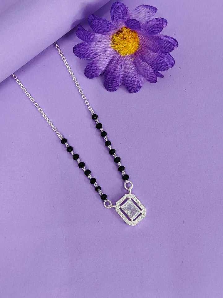 Necklace with a black beaded chain and silver pendant on a purple background with a purple flower.