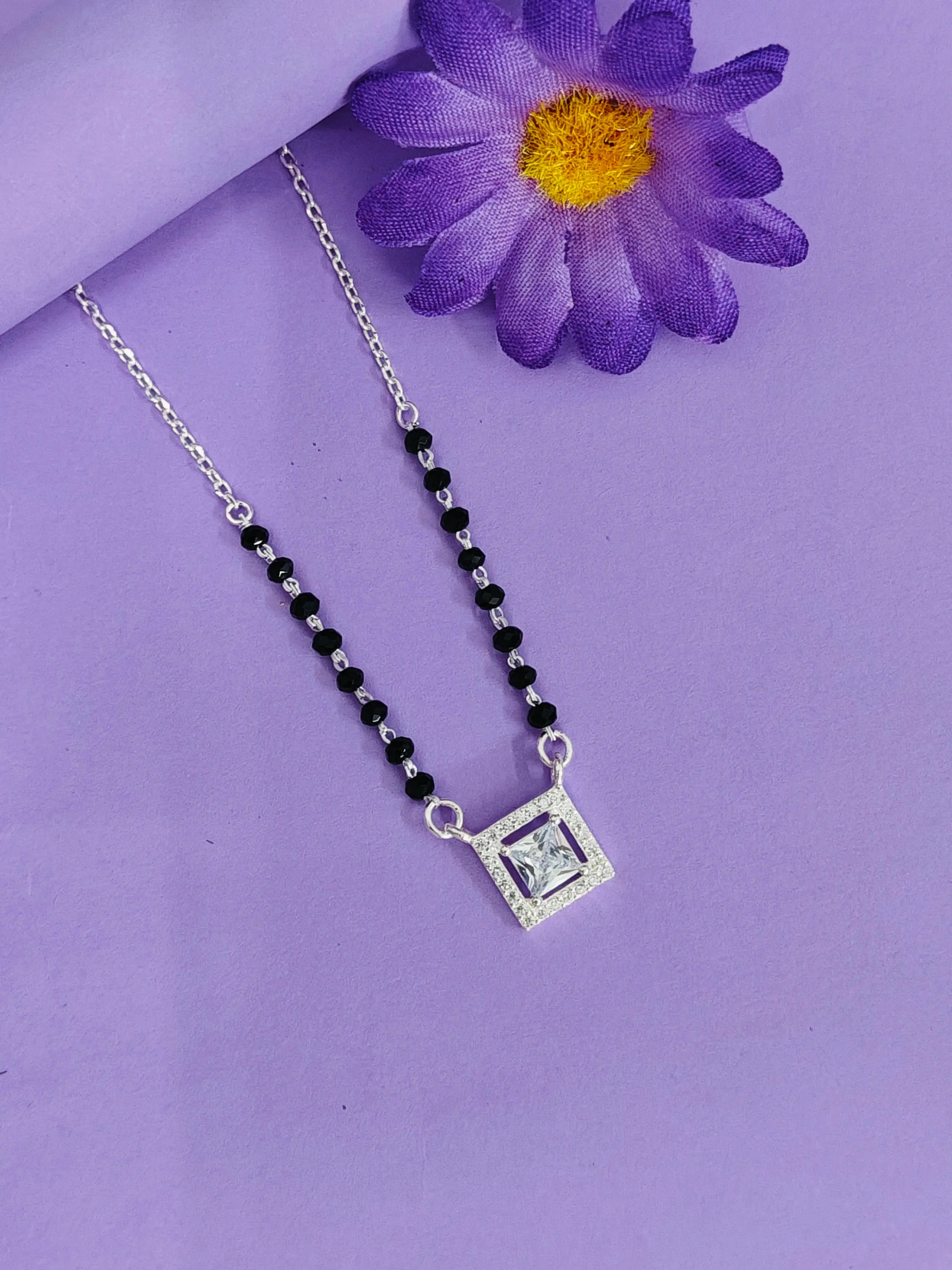 Necklace with black beads and silver square pendant on a purple background with a purple flower.