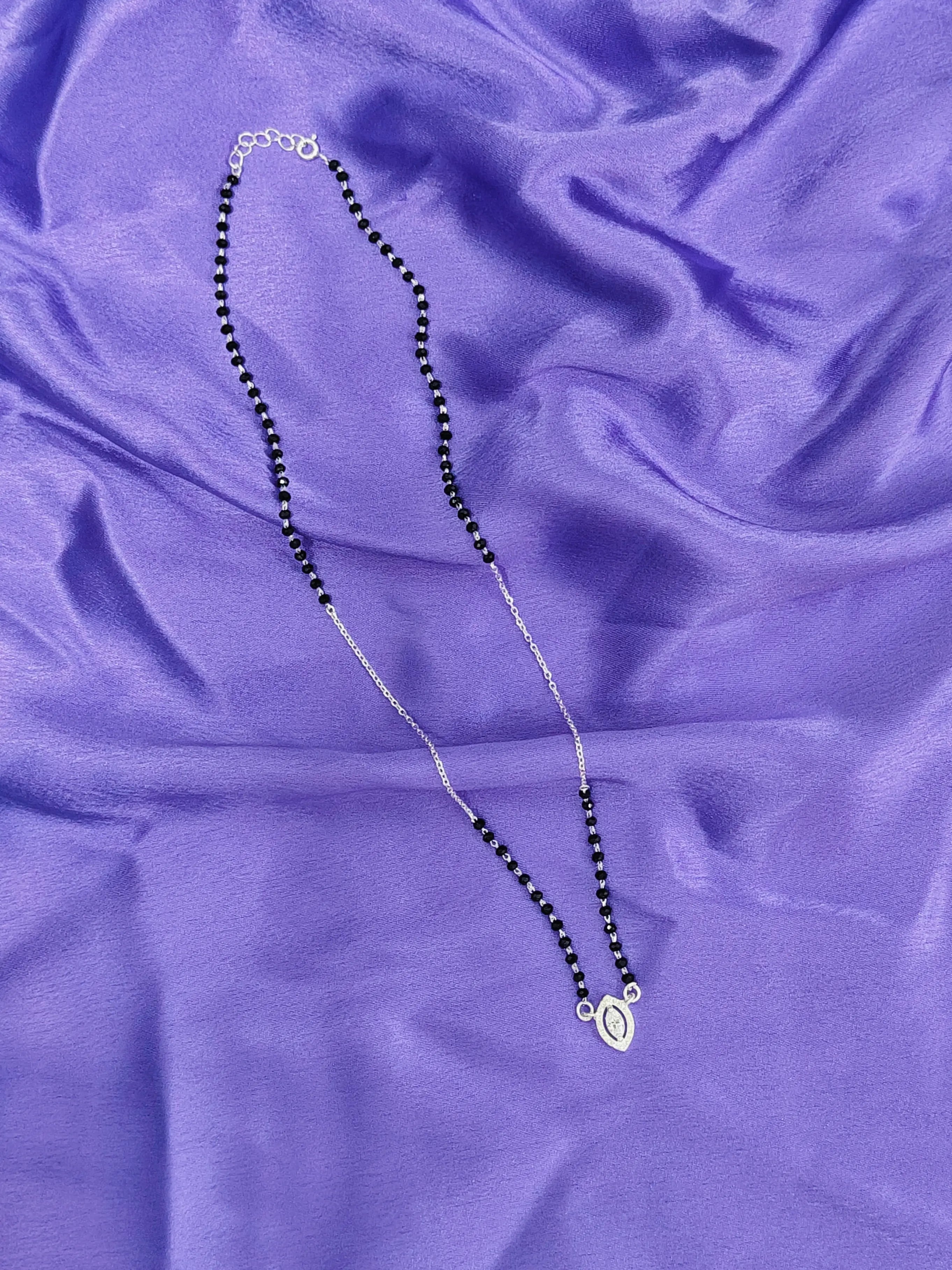 Necklace with black beads and a silver clasp on a purple fabric background