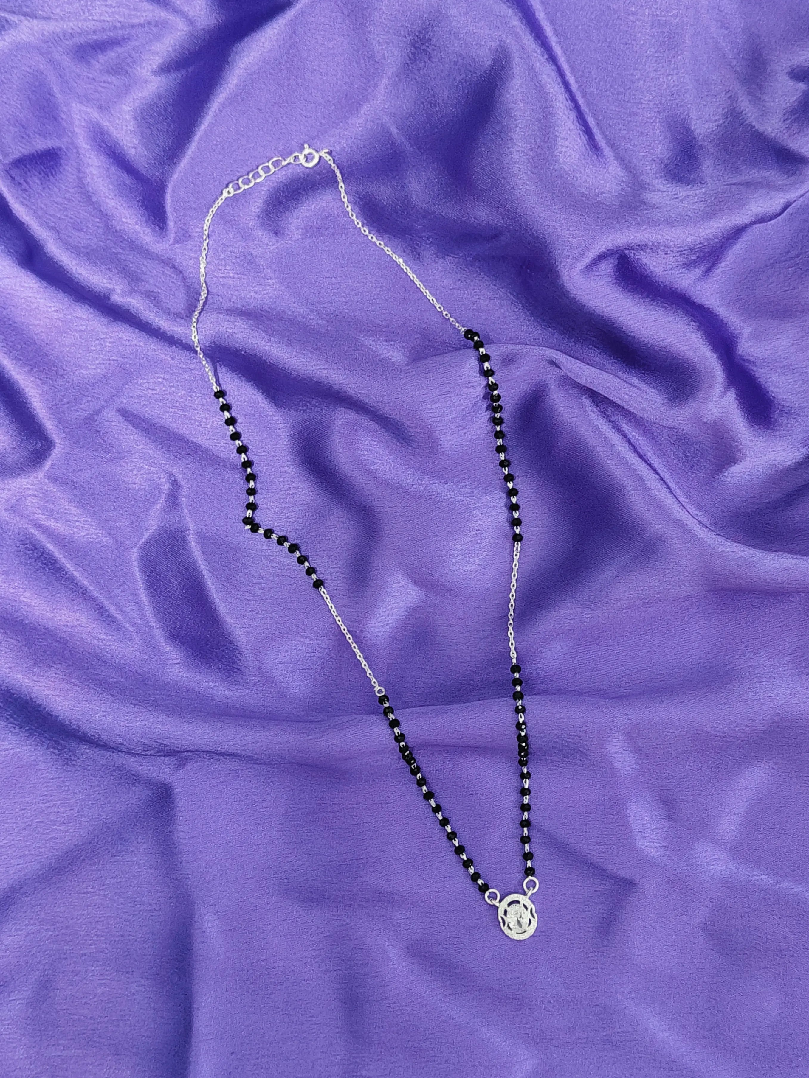 Necklace with black beads and a silver clasp on a purple fabric background