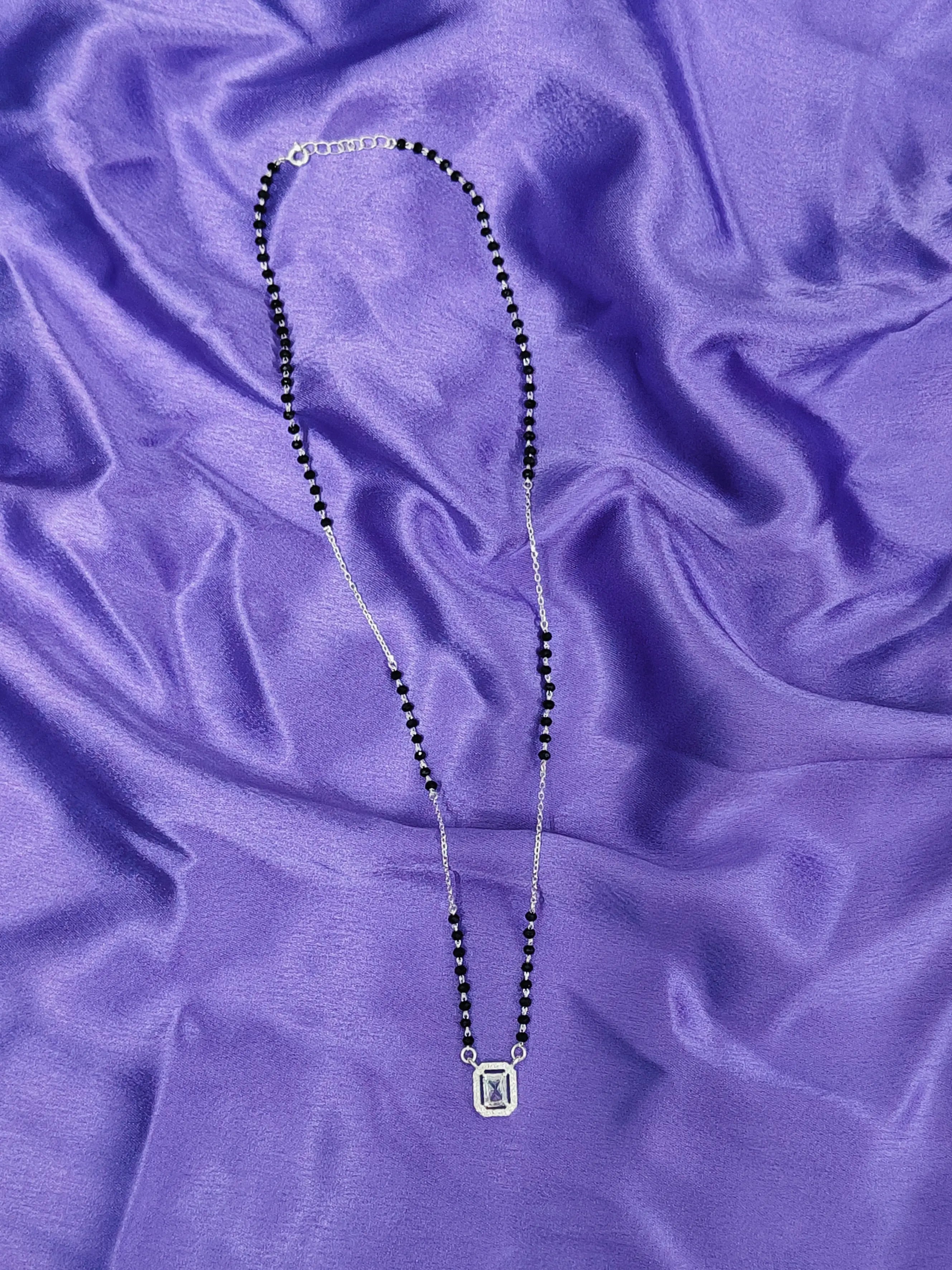 Necklace with black beads and a silver pendant on a purple fabric background