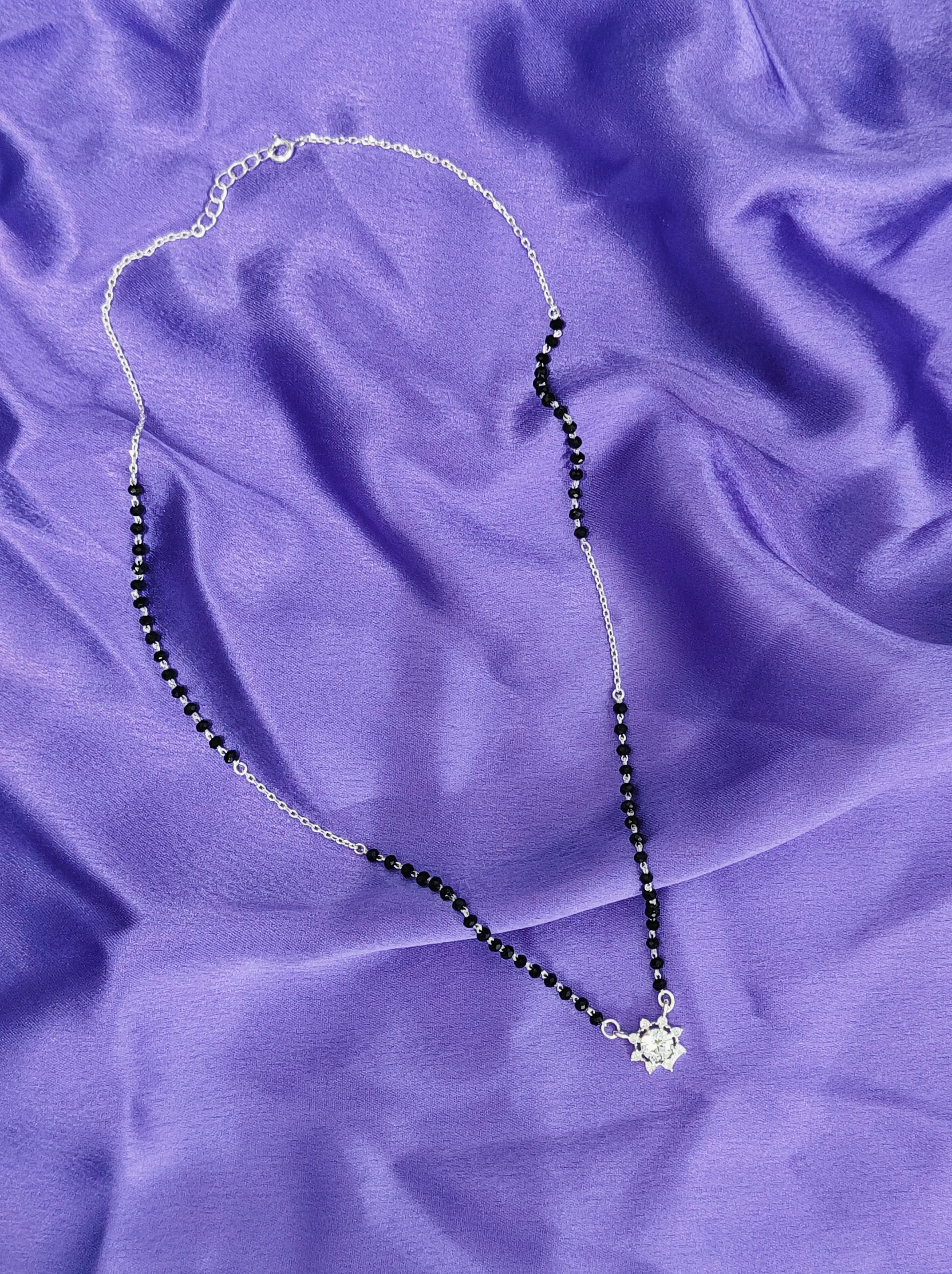 Necklace with black beads and a silver clasp on a purple fabric background