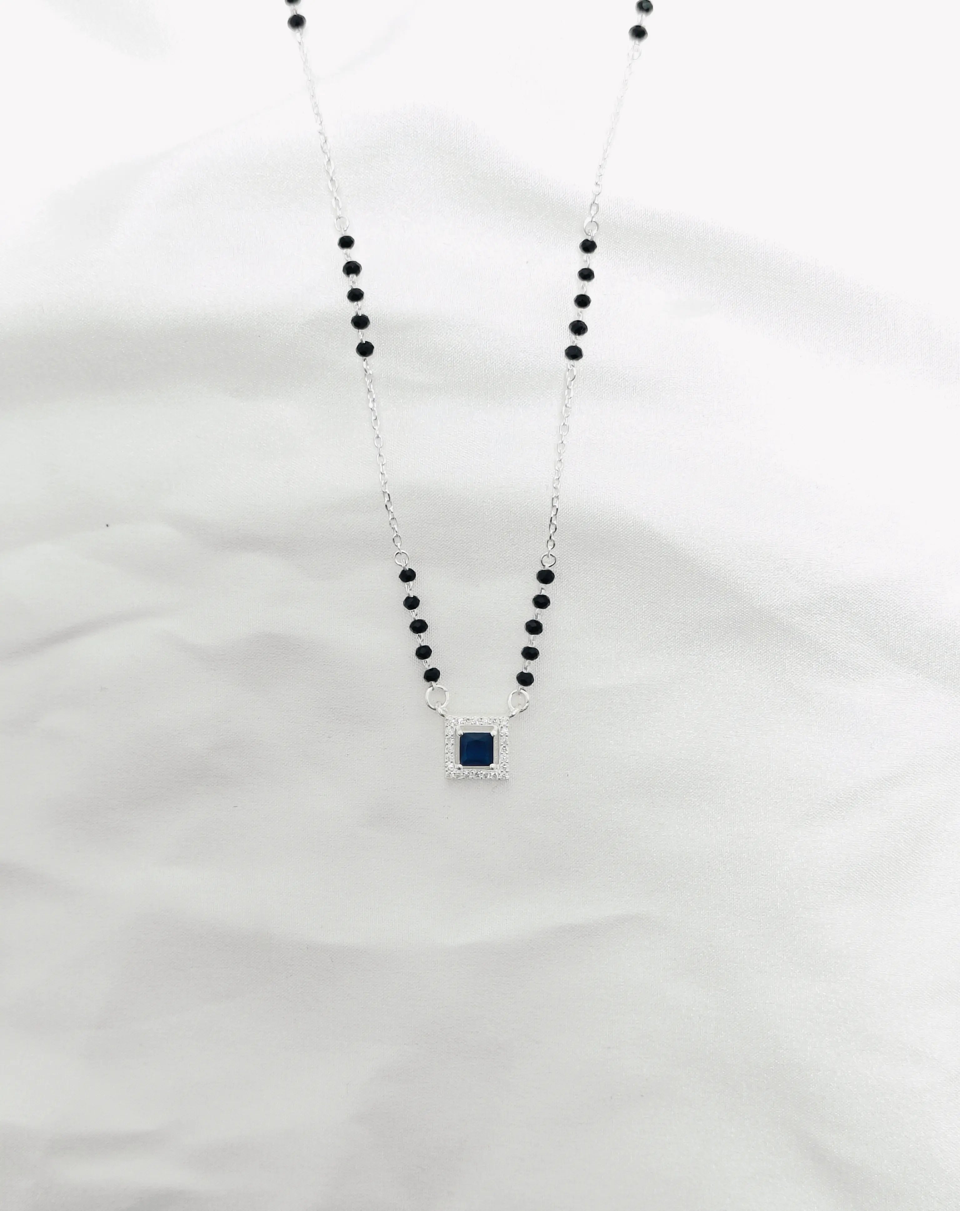 Necklace with black beads and a blue pendant on a white background