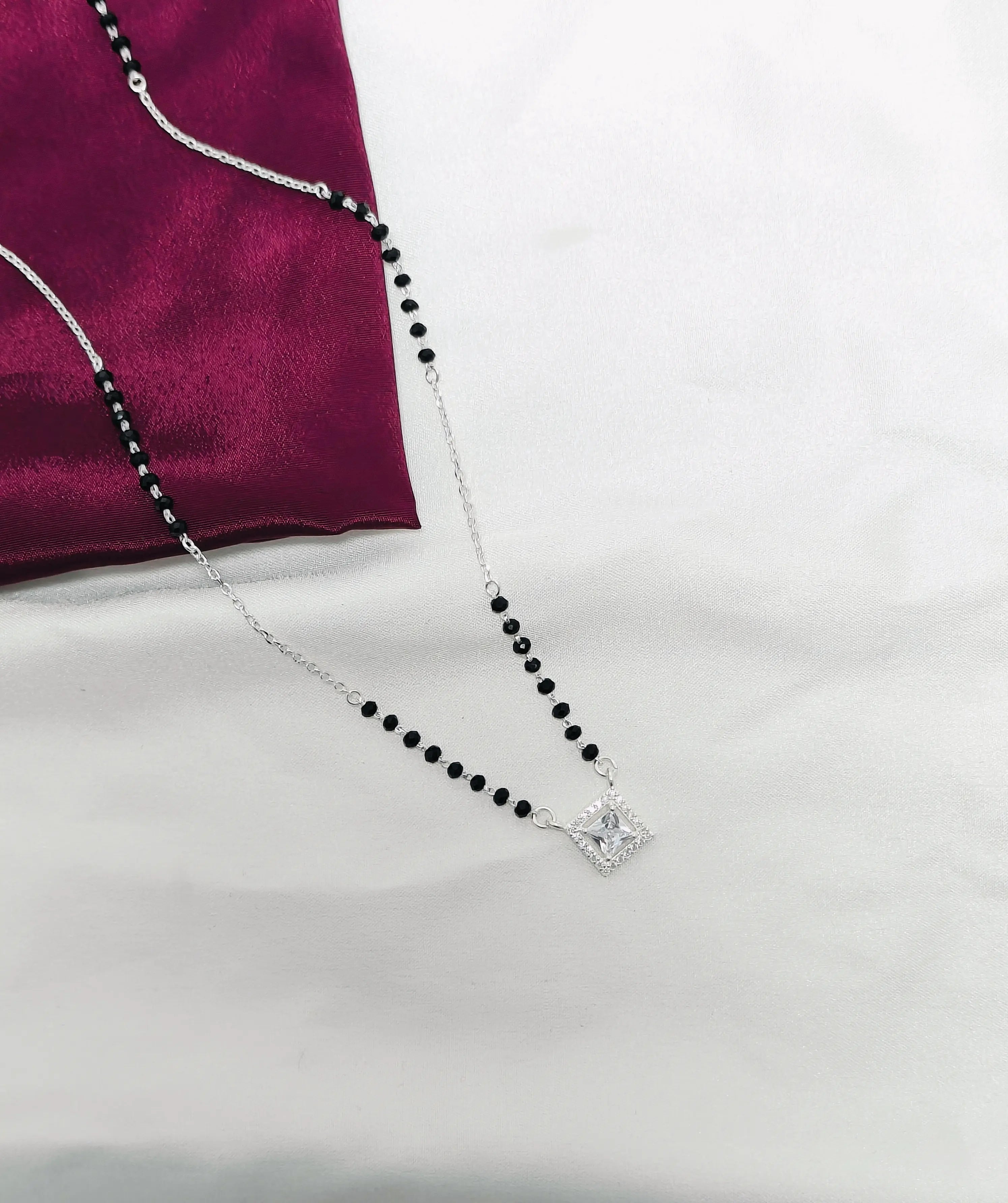 Necklace with black beads and a diamond pendant on a white surface