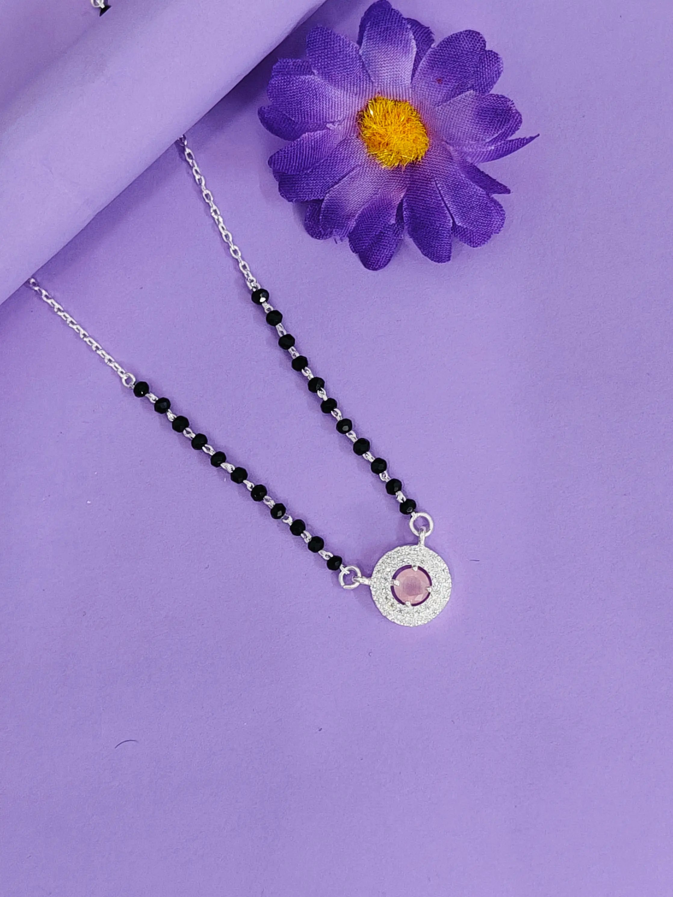 Necklace with black beads and a silver pendant on a purple background with a purple flower.
