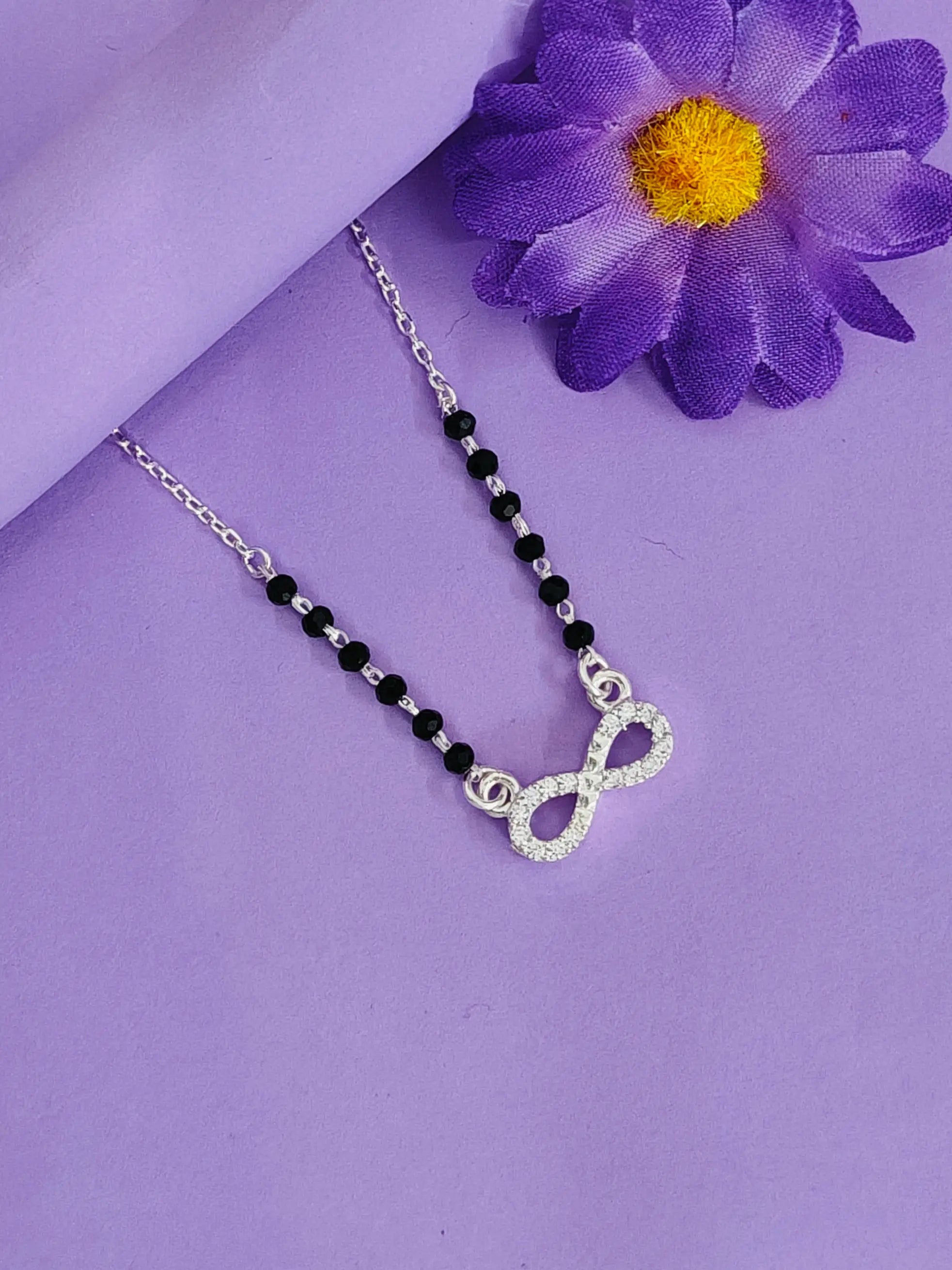 Necklace with black beads and silver infinity symbol pendant on a purple background with a purple flower.