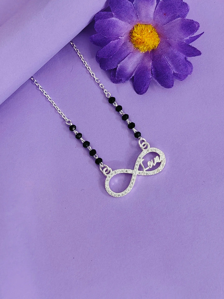 Necklace with infinity and heart pendant on a purple background with a purple flower.