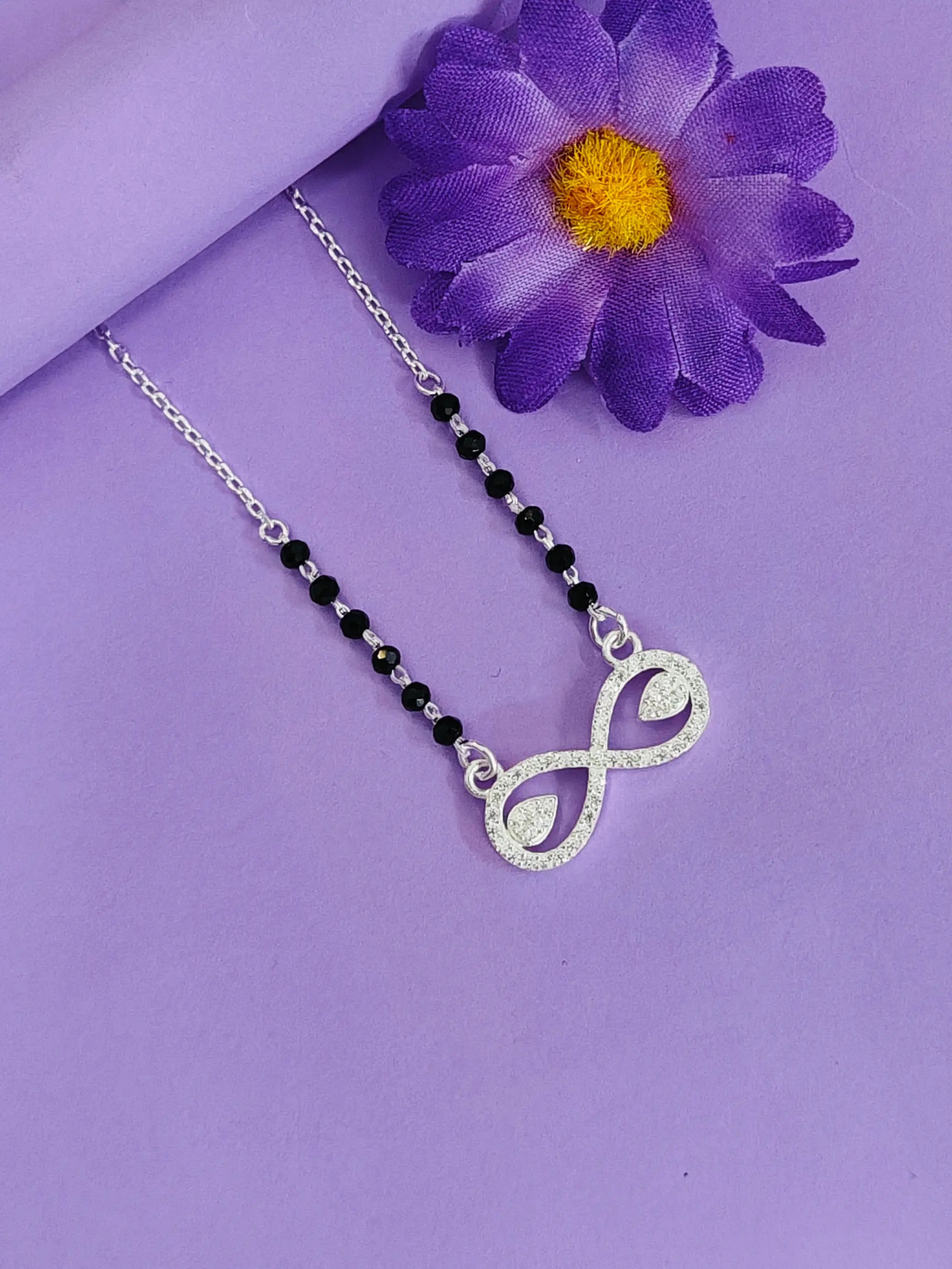 Necklace with an infinity symbol pendant on a purple background with a purple flower.