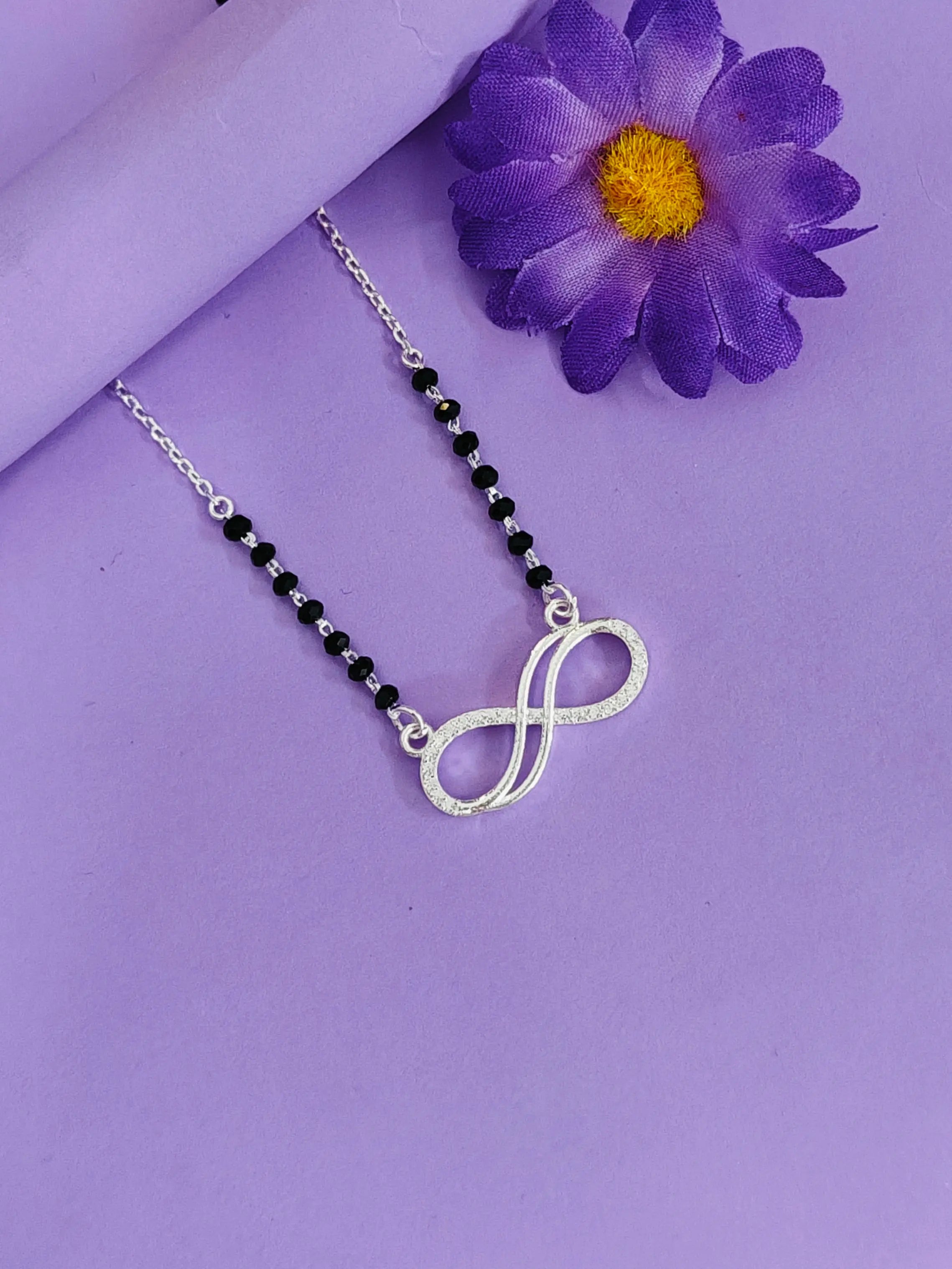 Necklace with infinity symbol pendant on a purple background with a purple flower.