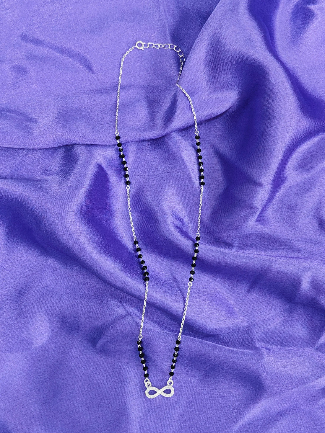 Necklace with a silver infinity symbol pendant on a purple fabric background