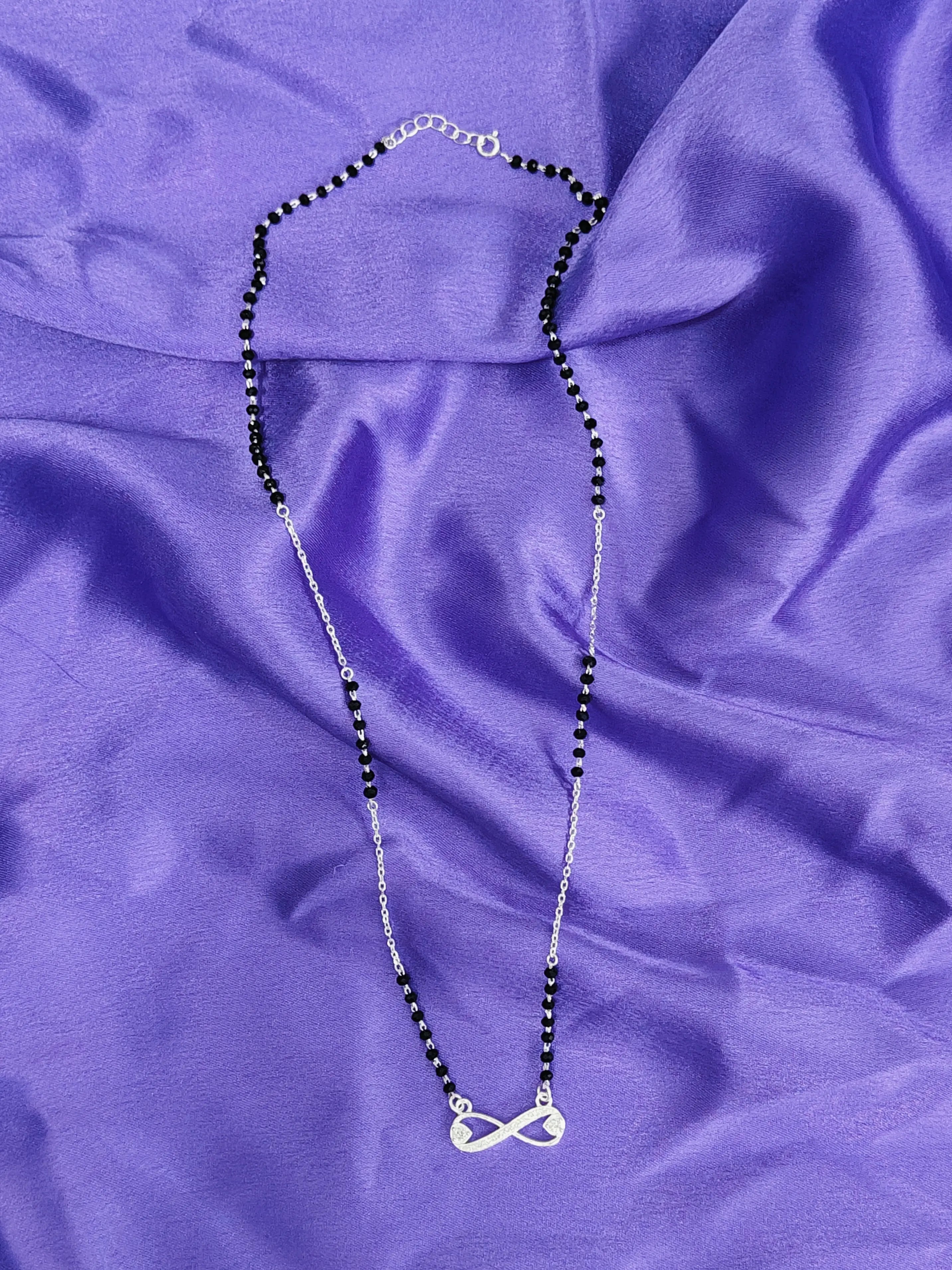 Necklace with black beads and a silver pendant on a purple fabric background