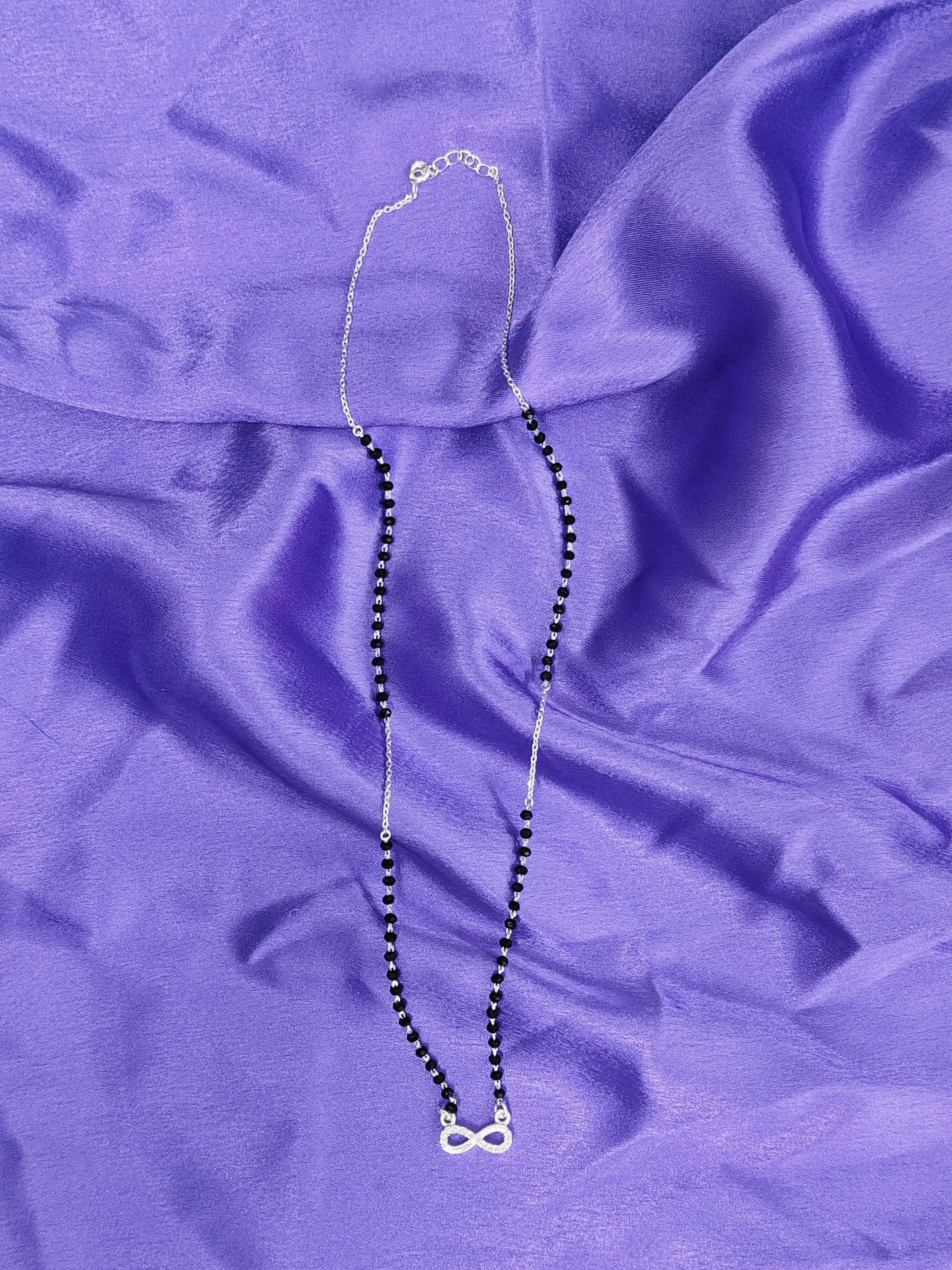 Necklace with a black beaded chain and silver clasp on a purple fabric background