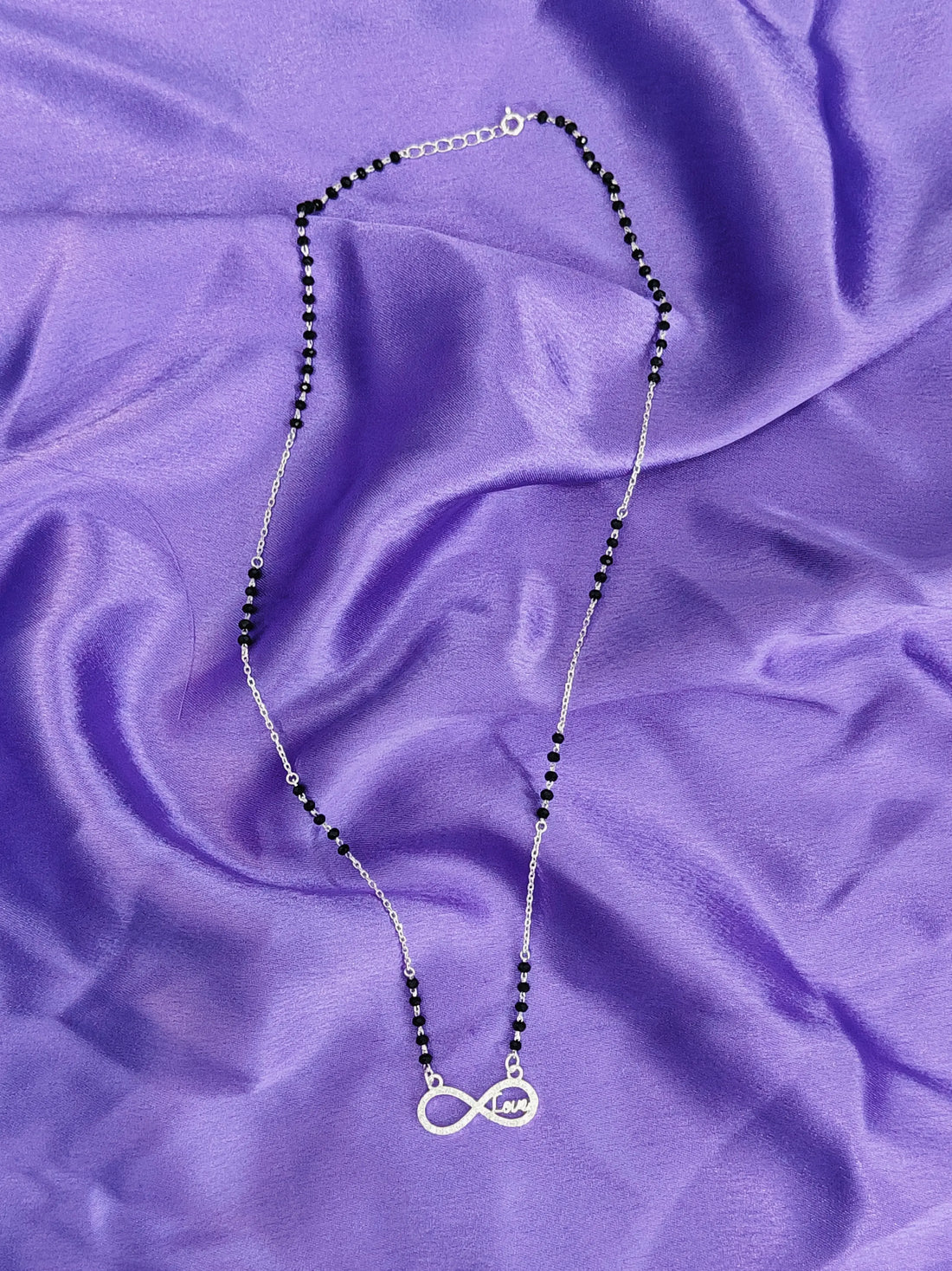 Necklace with black beads and a silver pendant on a purple fabric background