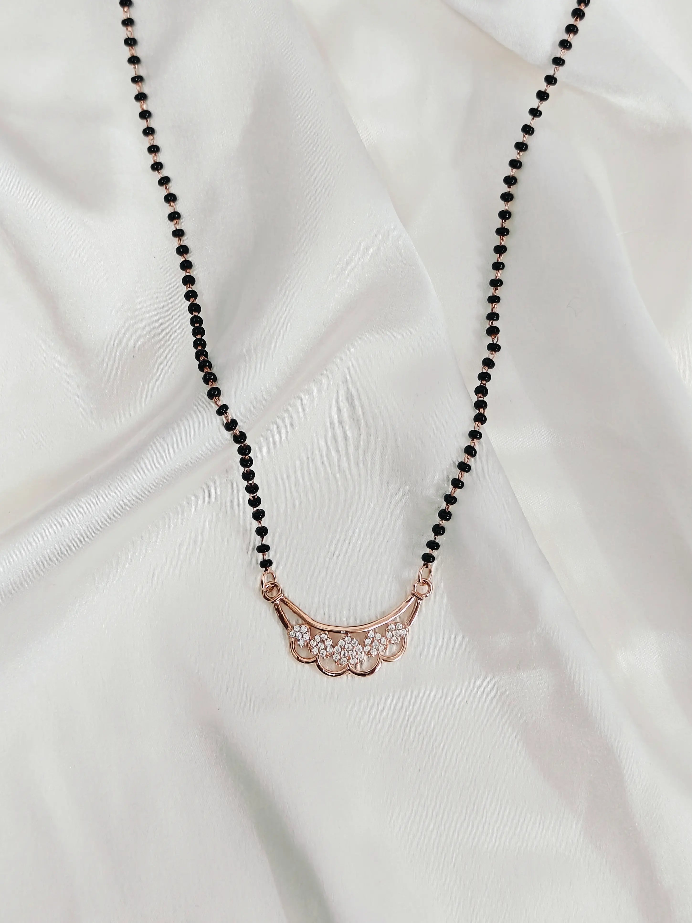 Necklace with black beads and a rose gold pendant on a white fabric background
