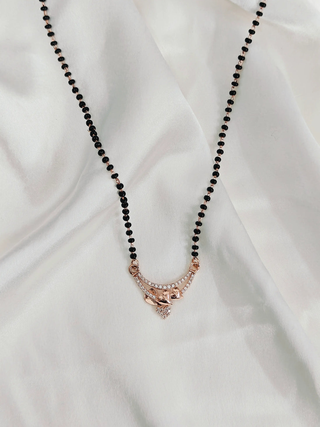 Necklace with black beads and a rose gold pendant on a white fabric background