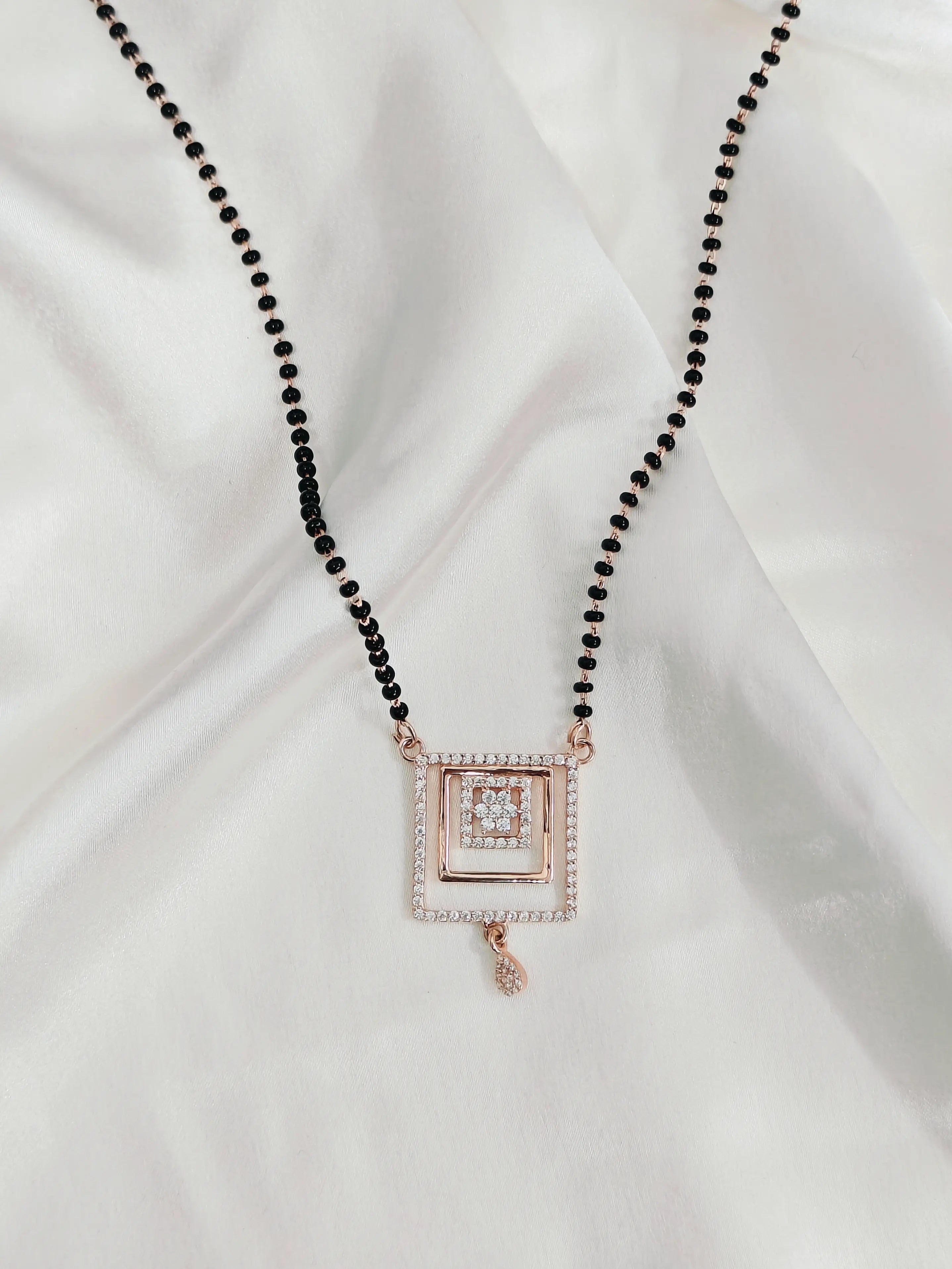 Necklace with black beads and a square pendant on a white fabric background