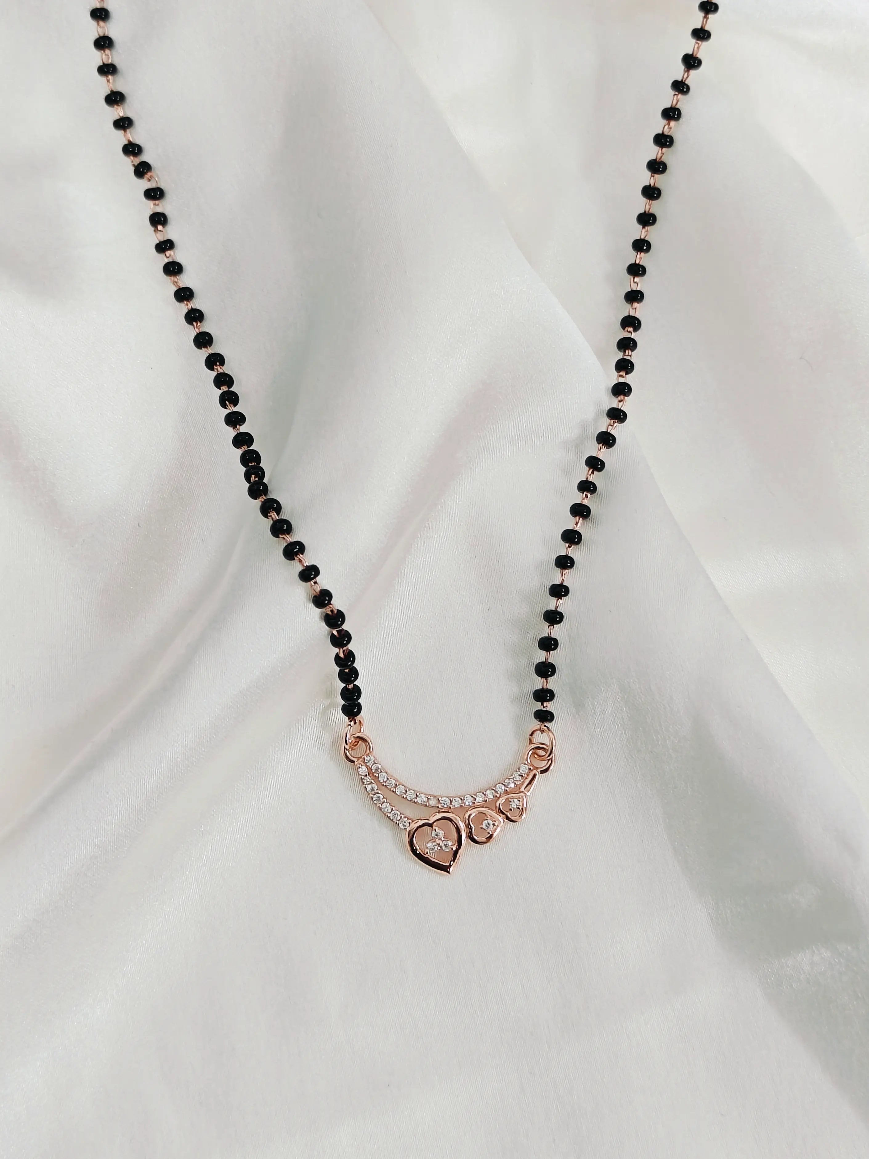 Necklace with black beads and a rose gold heart pendant on a white fabric background