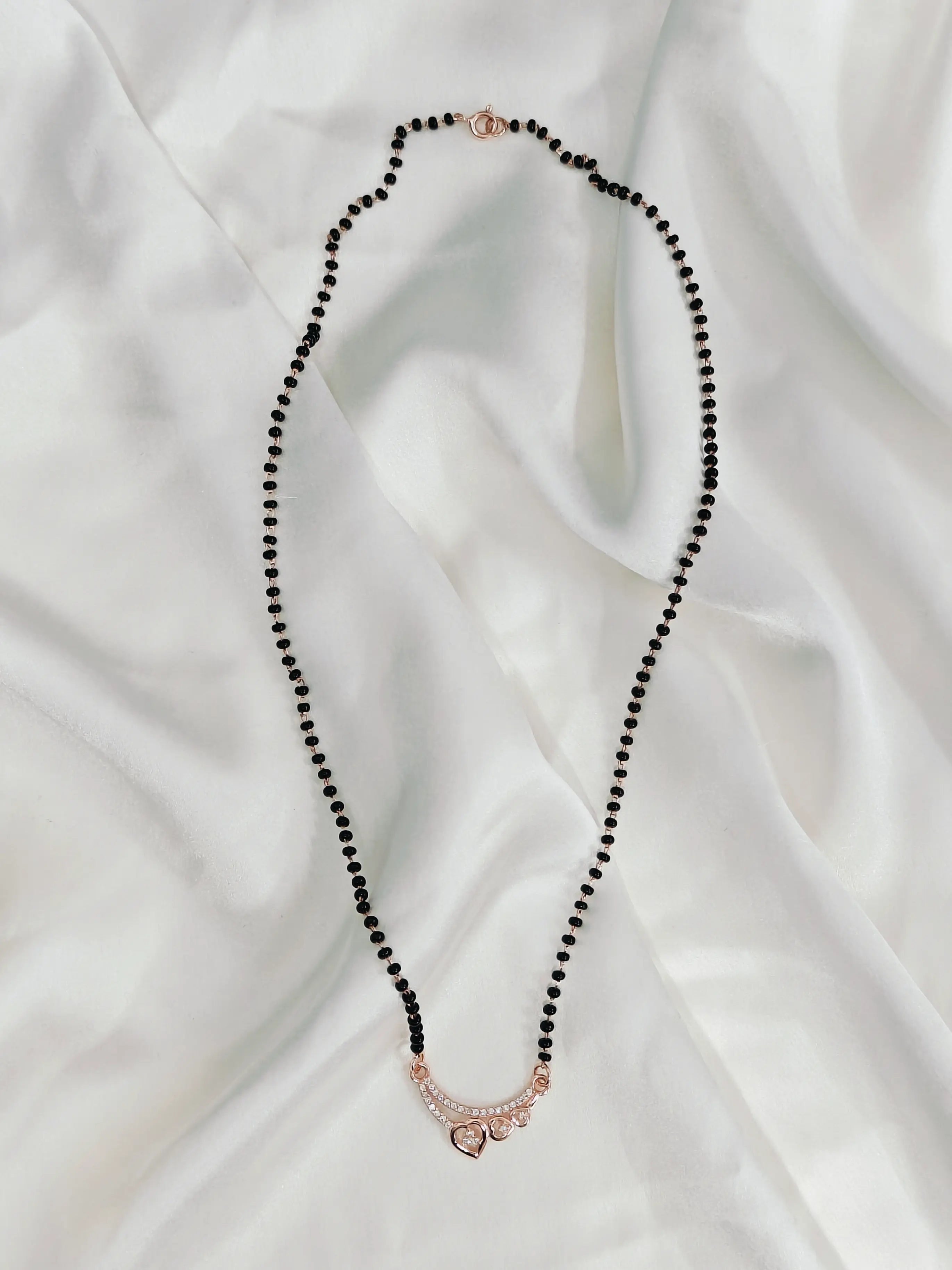 Necklace with black beads and a rose gold clasp on a white fabric background