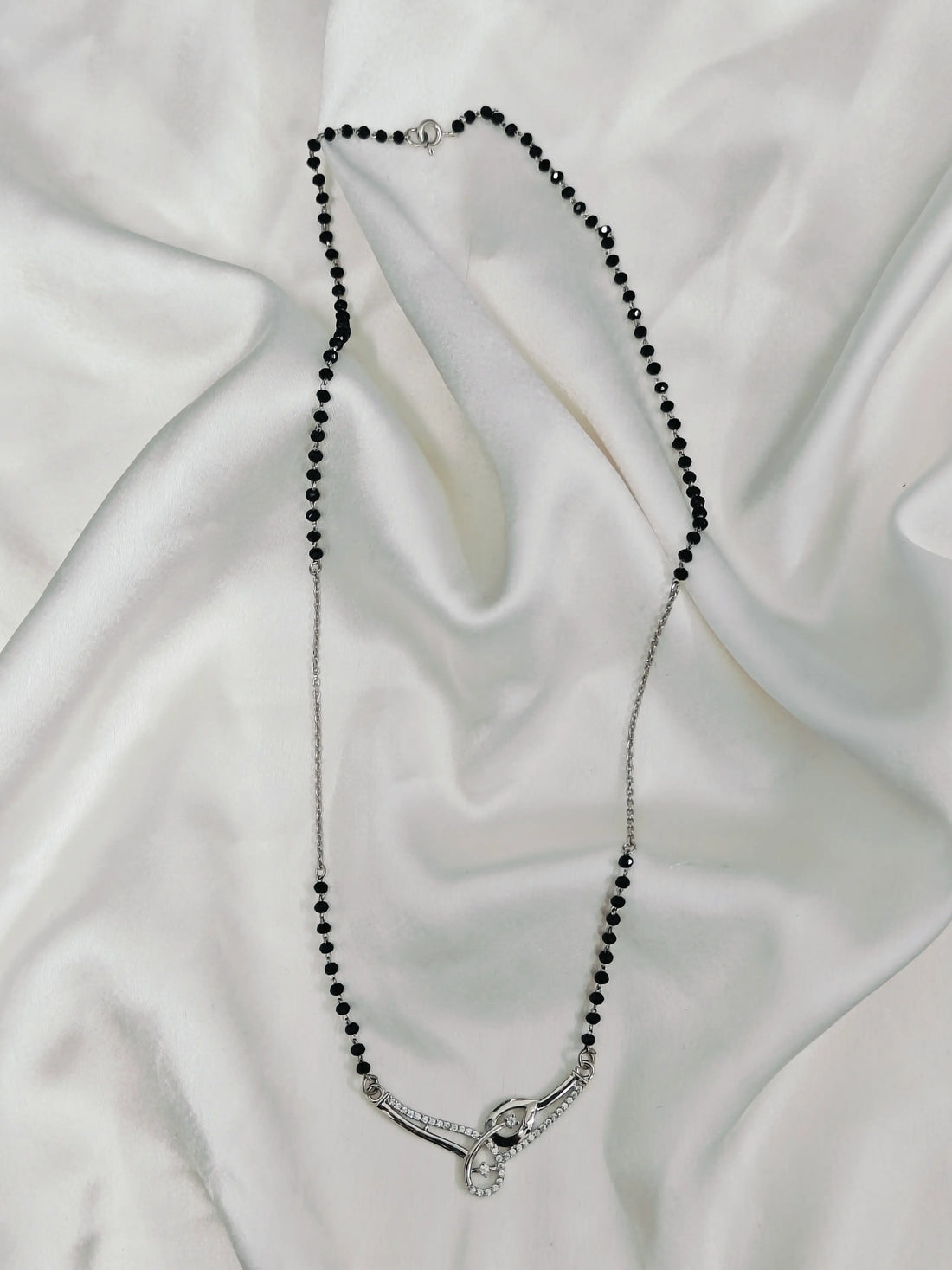 Necklace with black beads and a silver clasp on a white fabric background