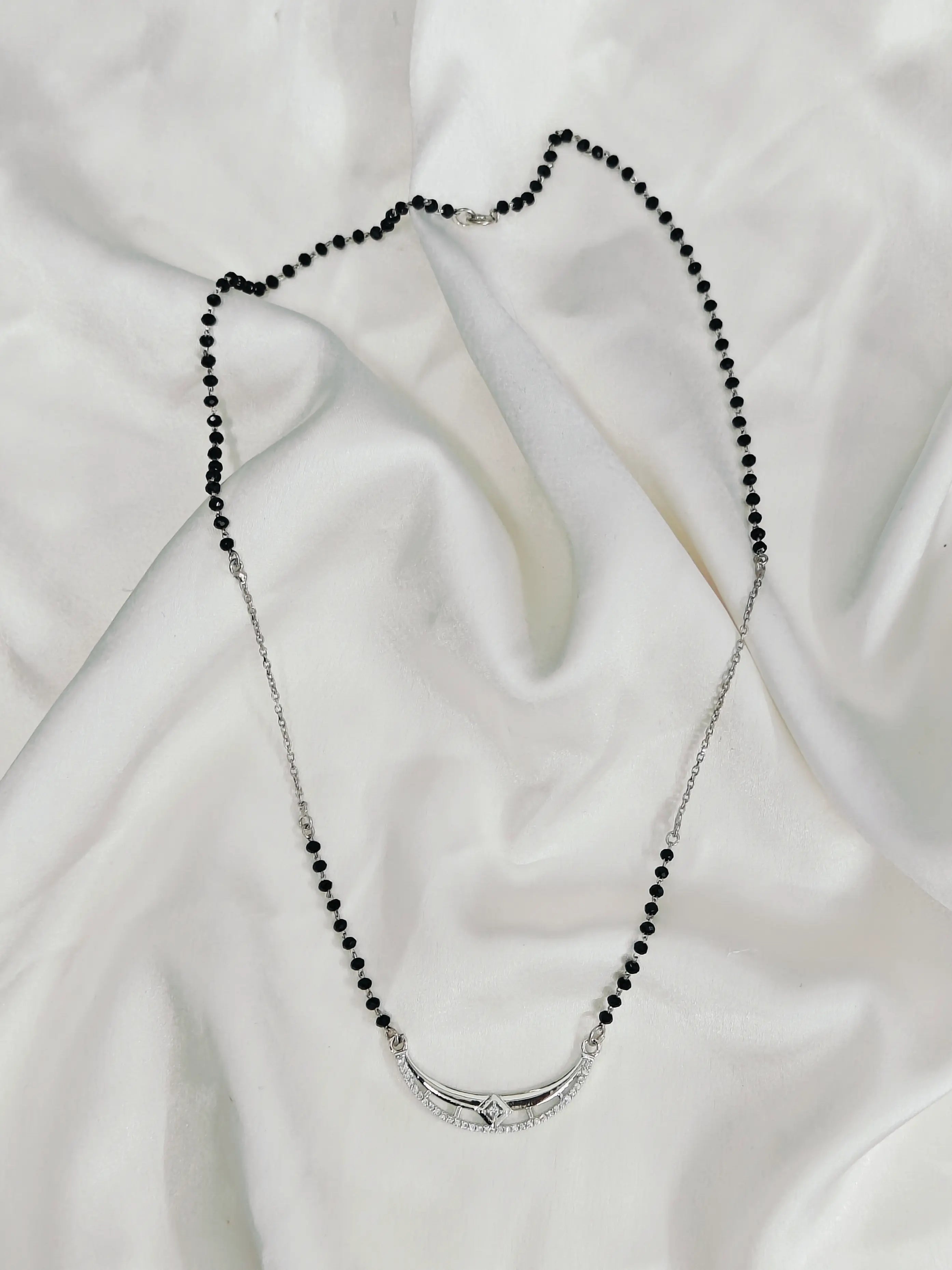 Necklace with black beads and silver clasp on a white fabric background
