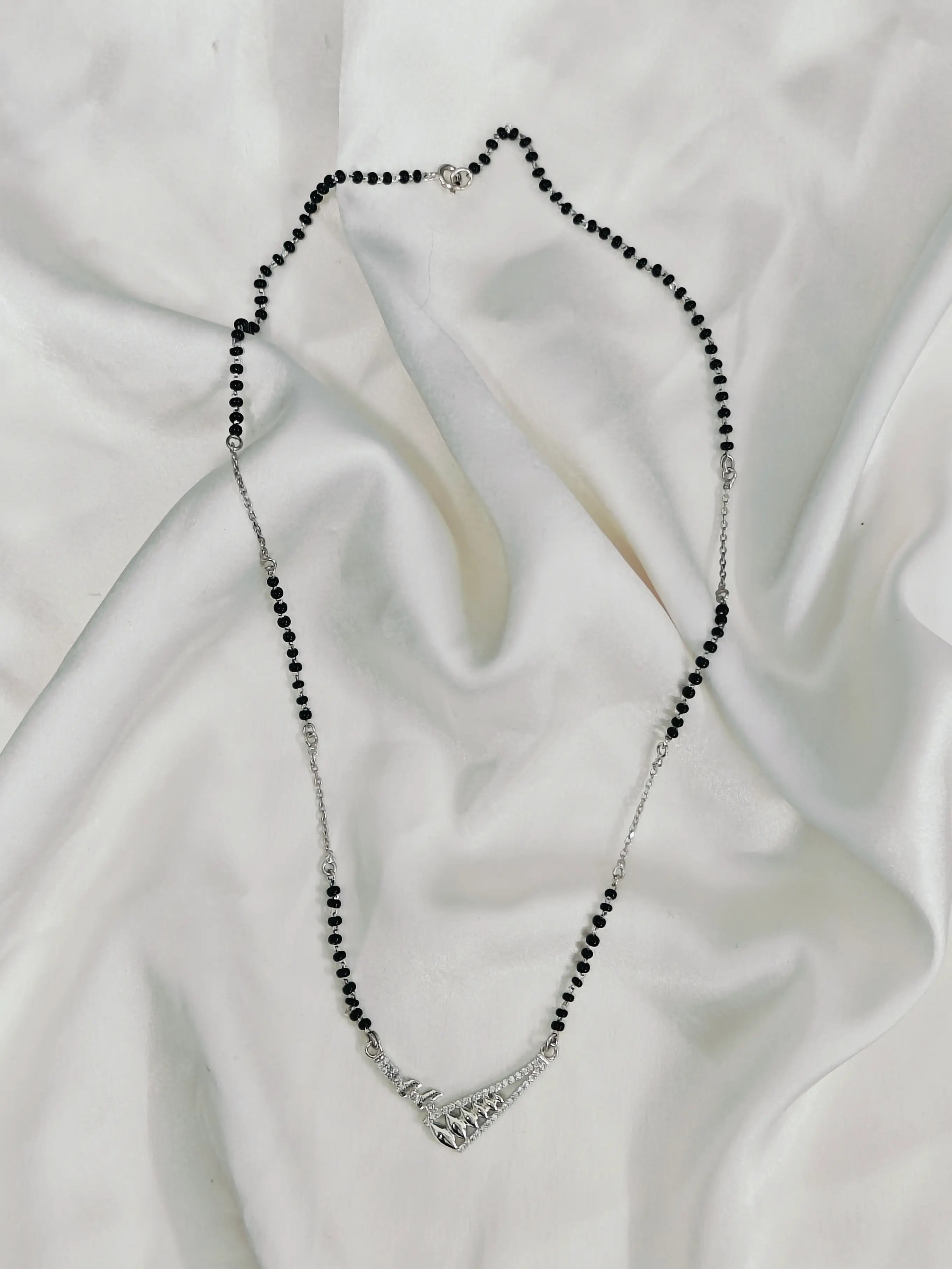 Necklace with black beads and silver clasp on a white fabric background