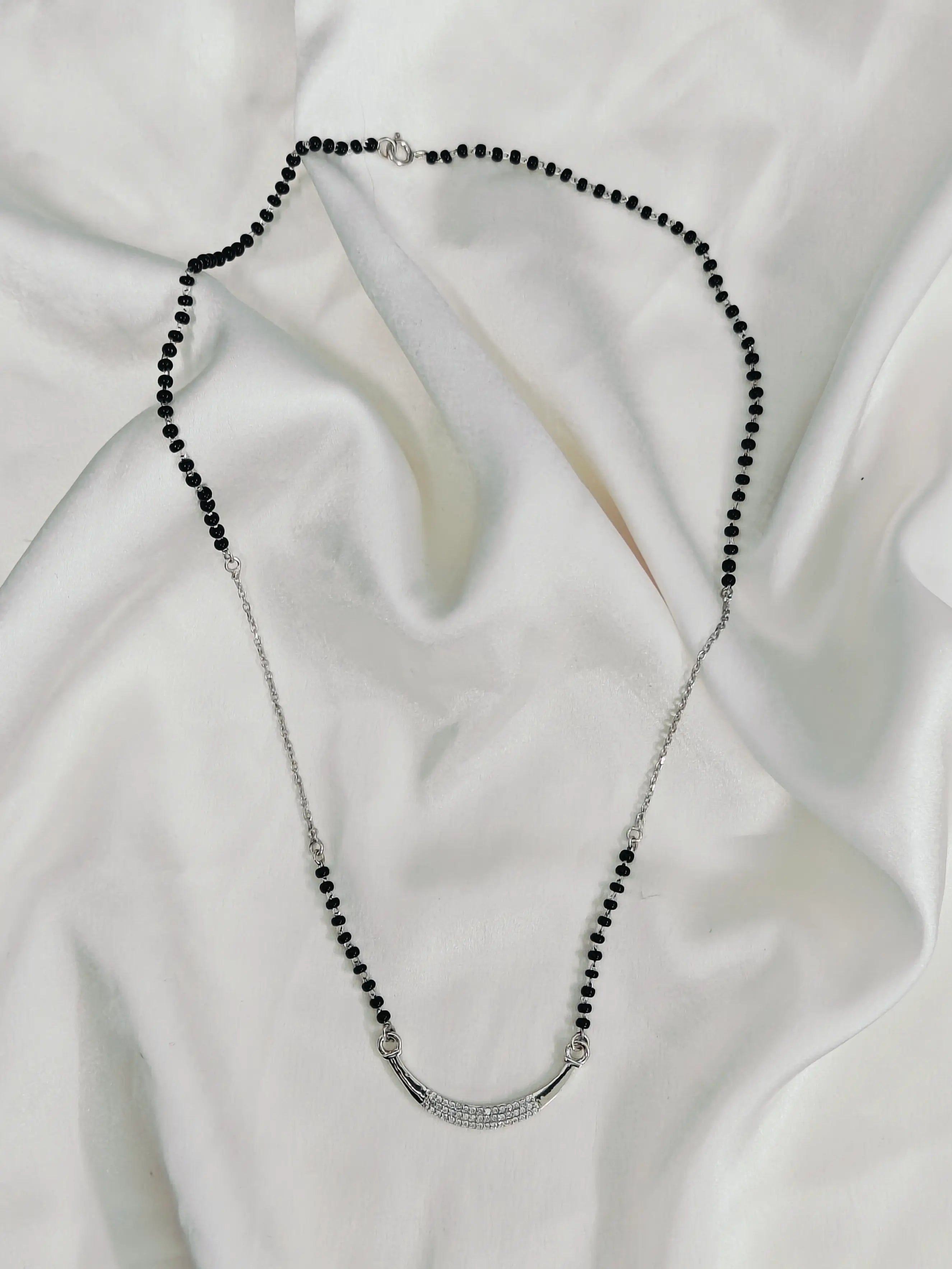 Necklace with black beads and silver clasp on a white fabric background