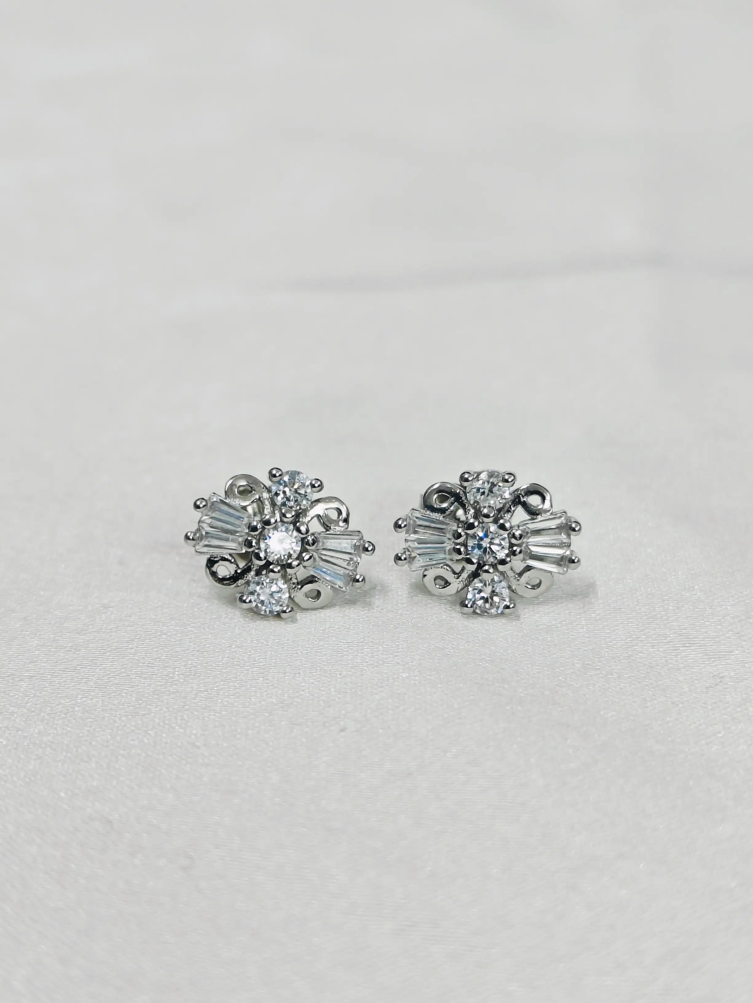 Pair of silver earrings with clear gemstones on a light gray background