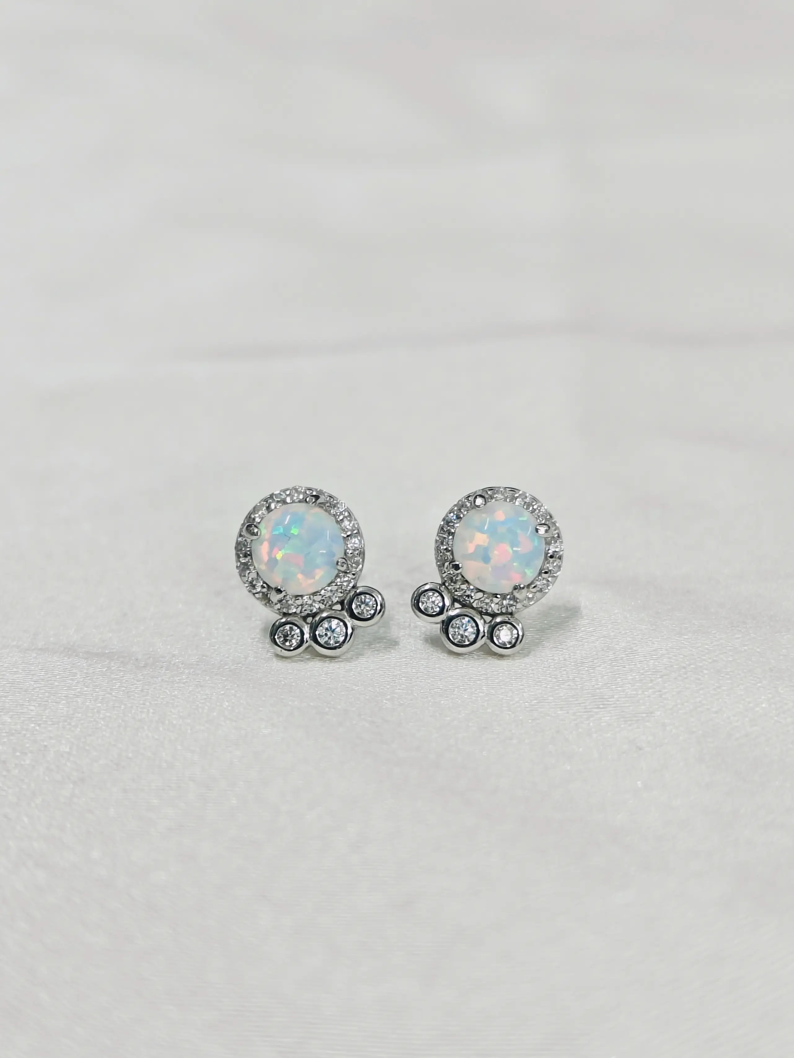 Pair of round opal earrings with silver accents on a light gray background