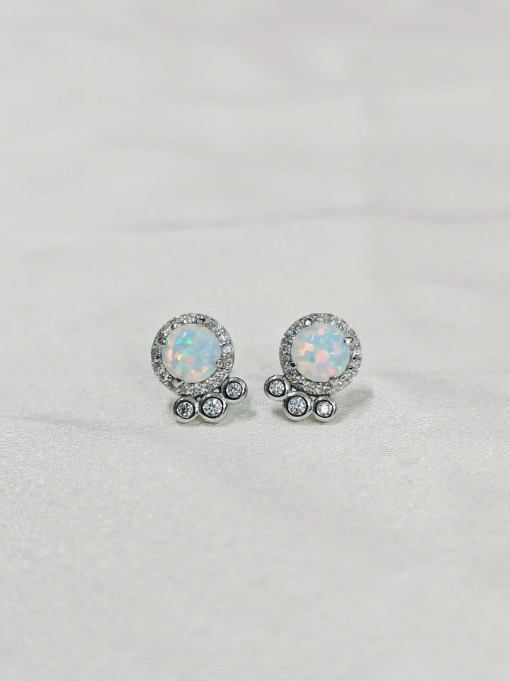 Pair of round opal earrings with silver accents on a light gray background