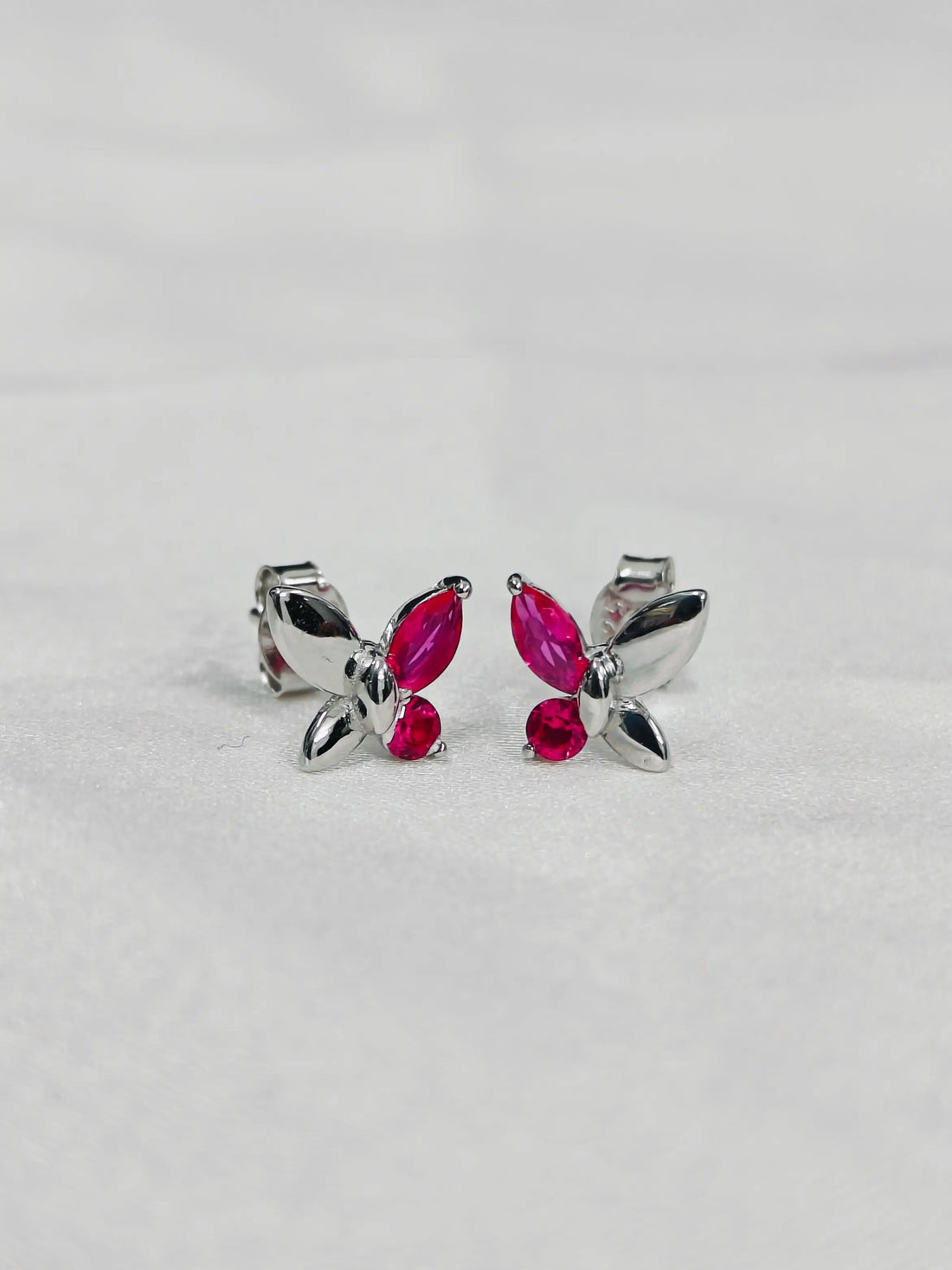 Butterfly-shaped earrings with pink gemstones on a light gray background