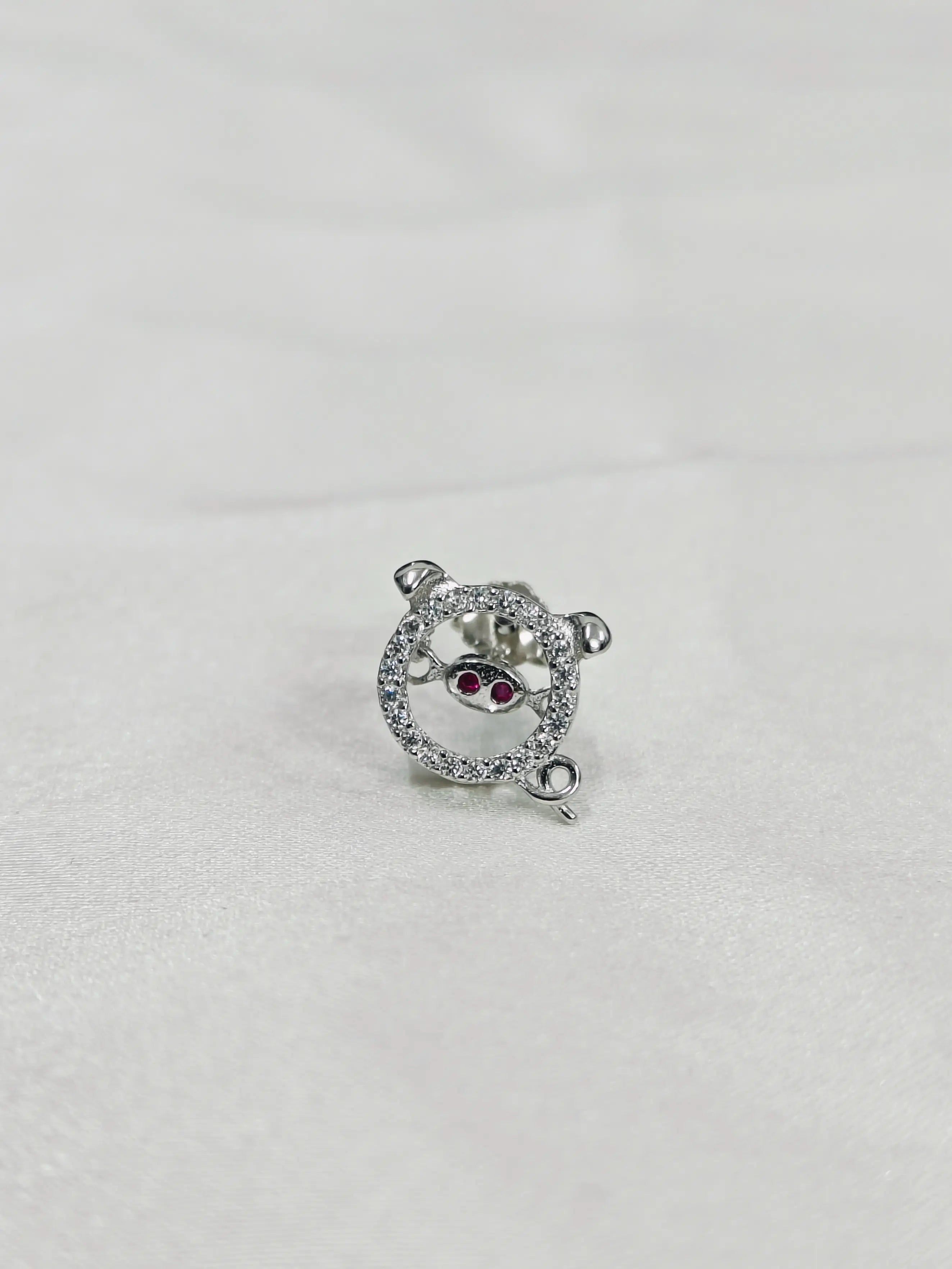 Silver teddy bear charm with red gemstones on a light gray background