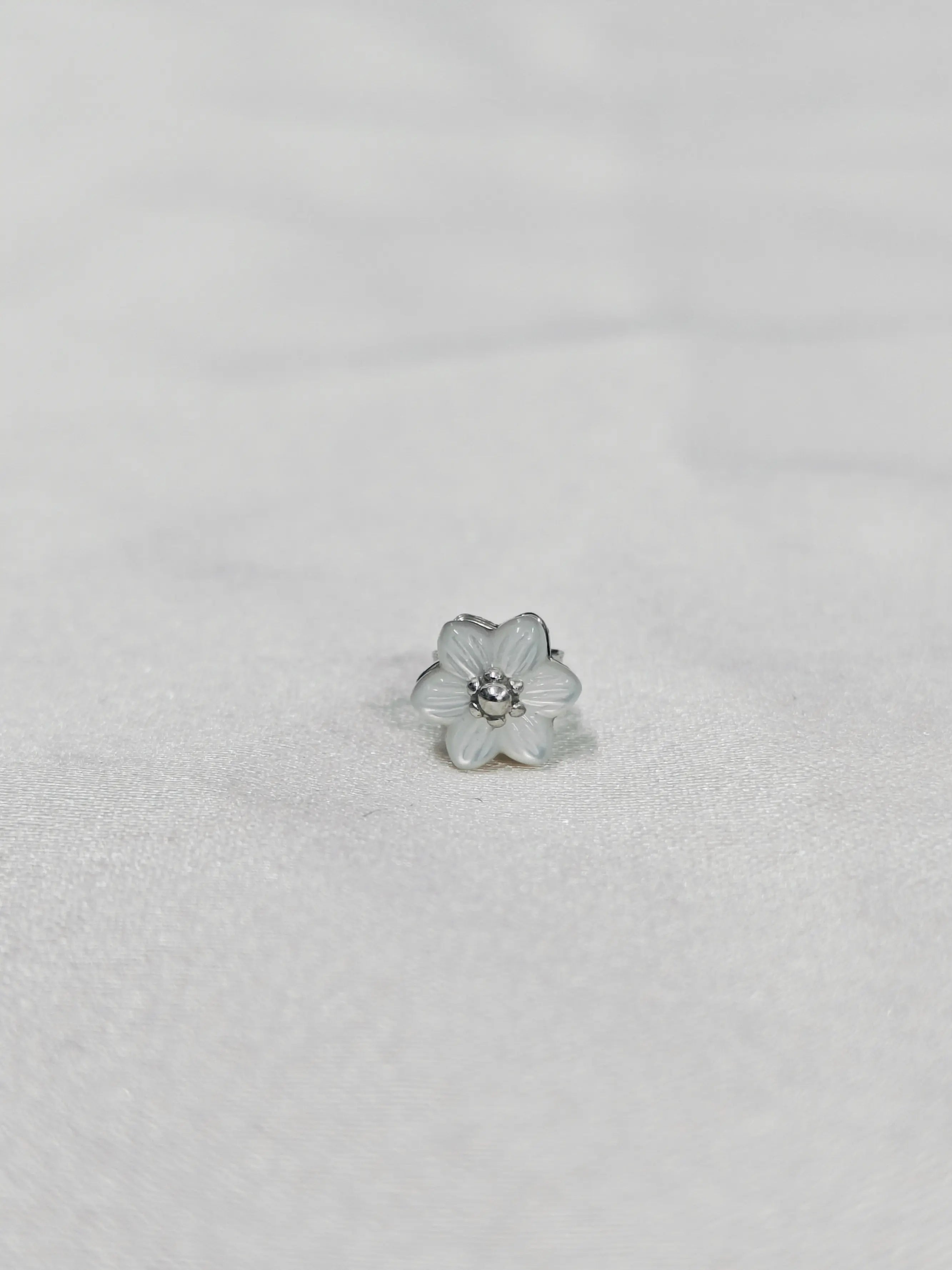 Silver flower-shaped earring on a light gray background
