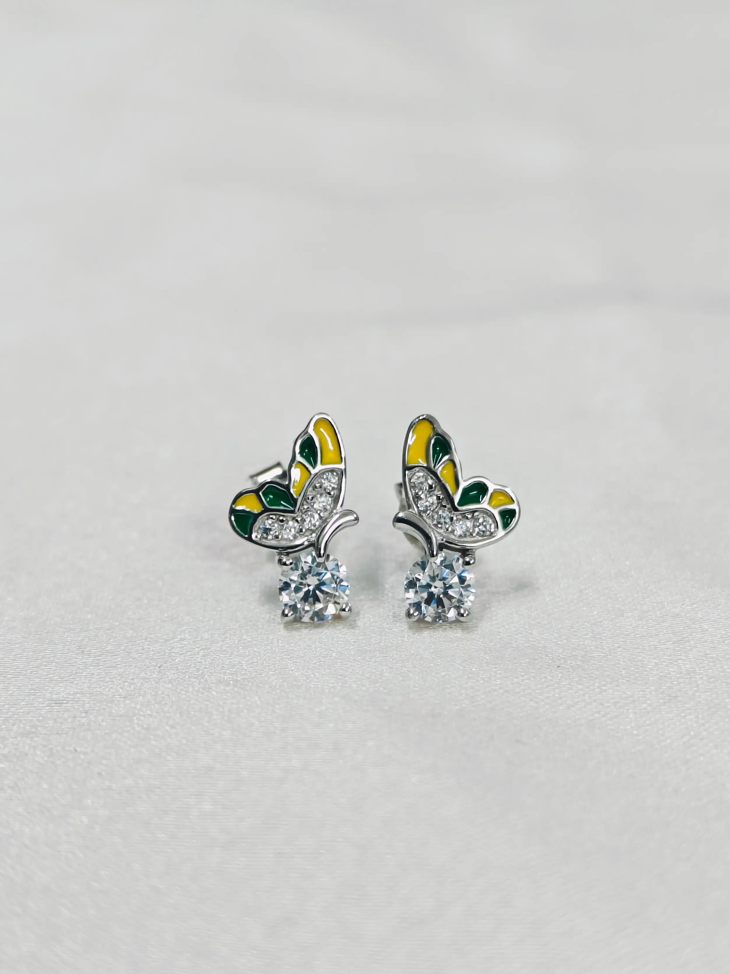 Butterfly-shaped earrings with green, yellow, and silver design on a light gray background