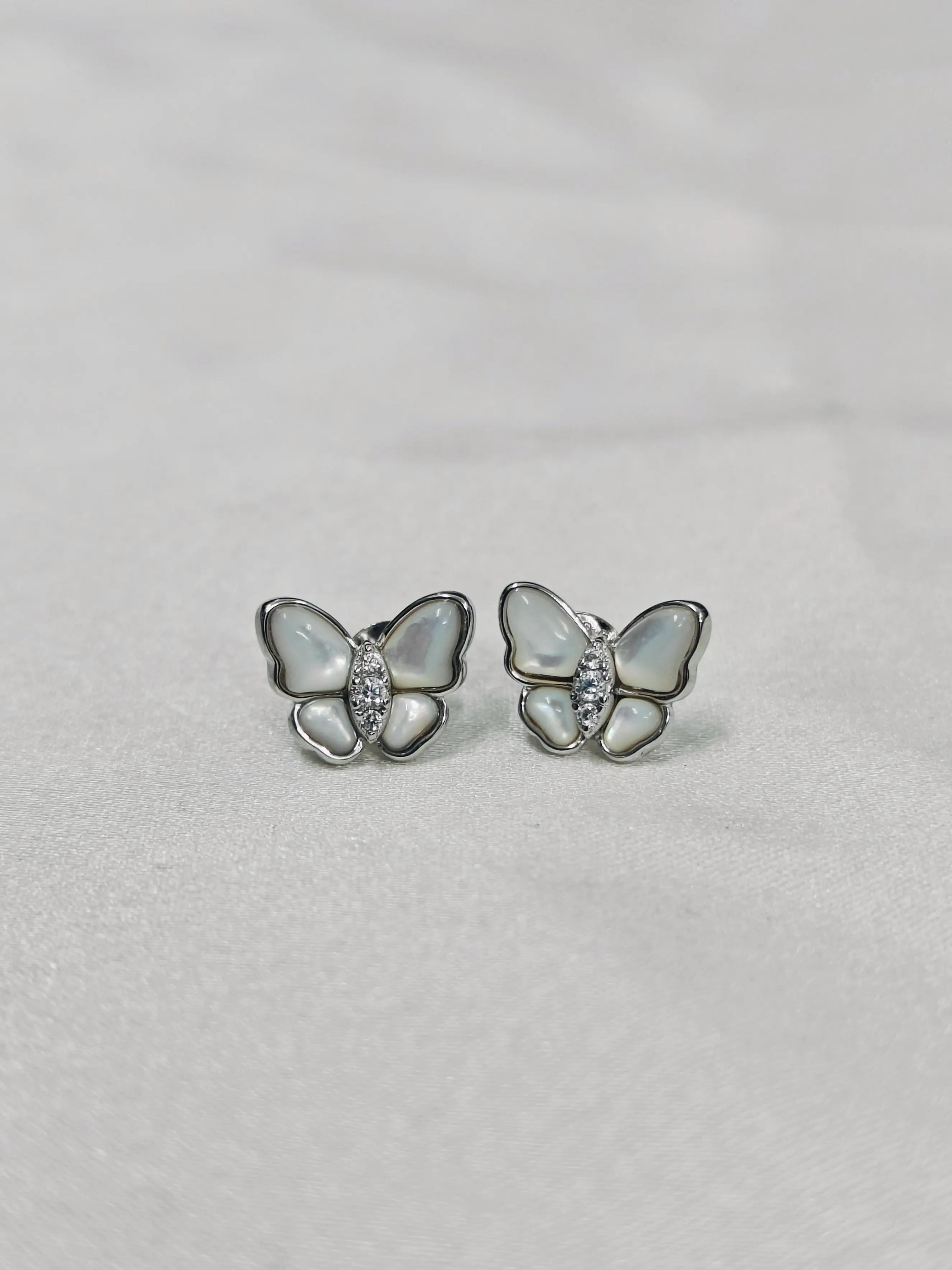 Butterfly-shaped earrings with gemstones on a light gray background