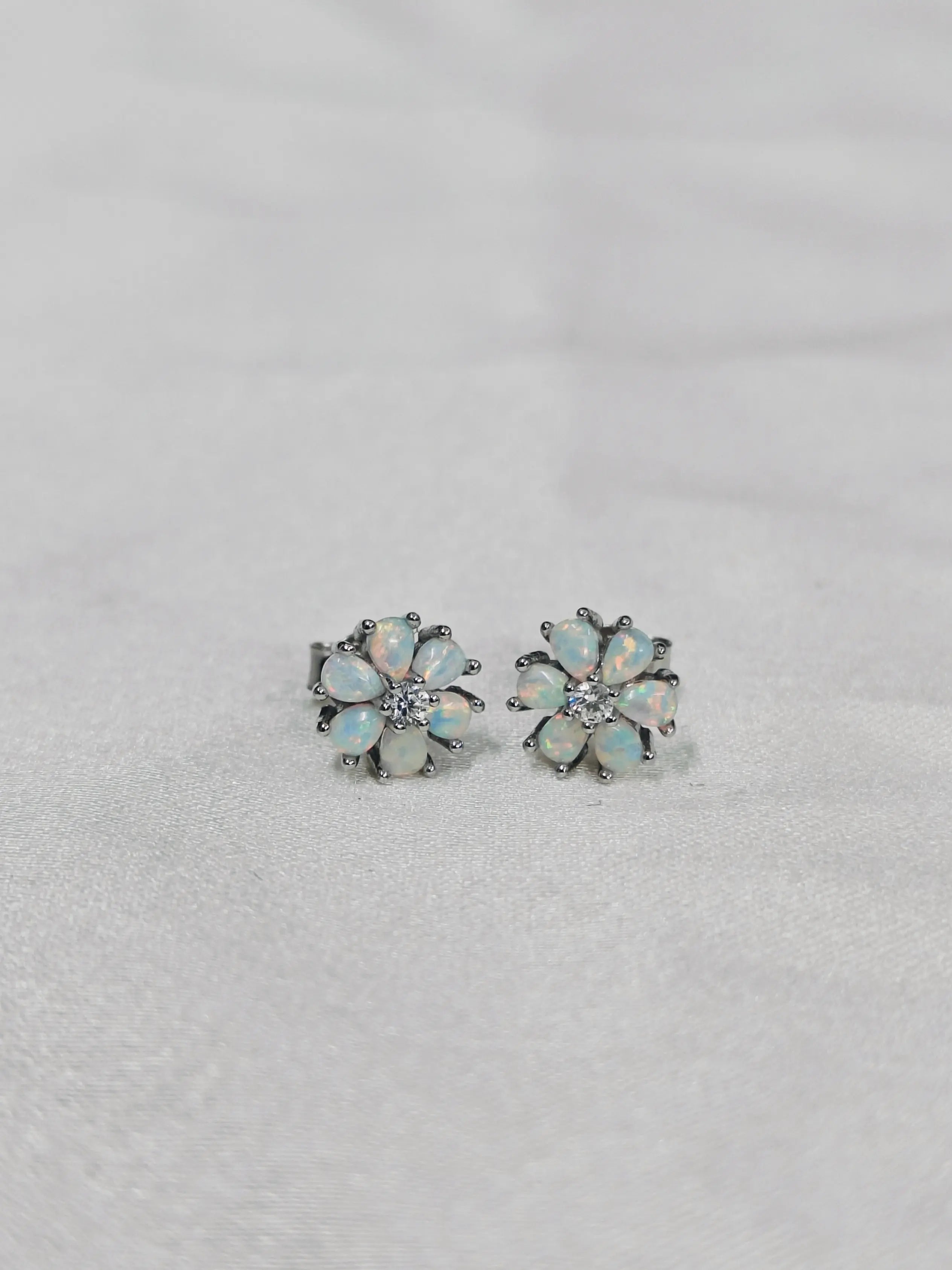 Pair of flower-shaped opal earrings on a light gray background