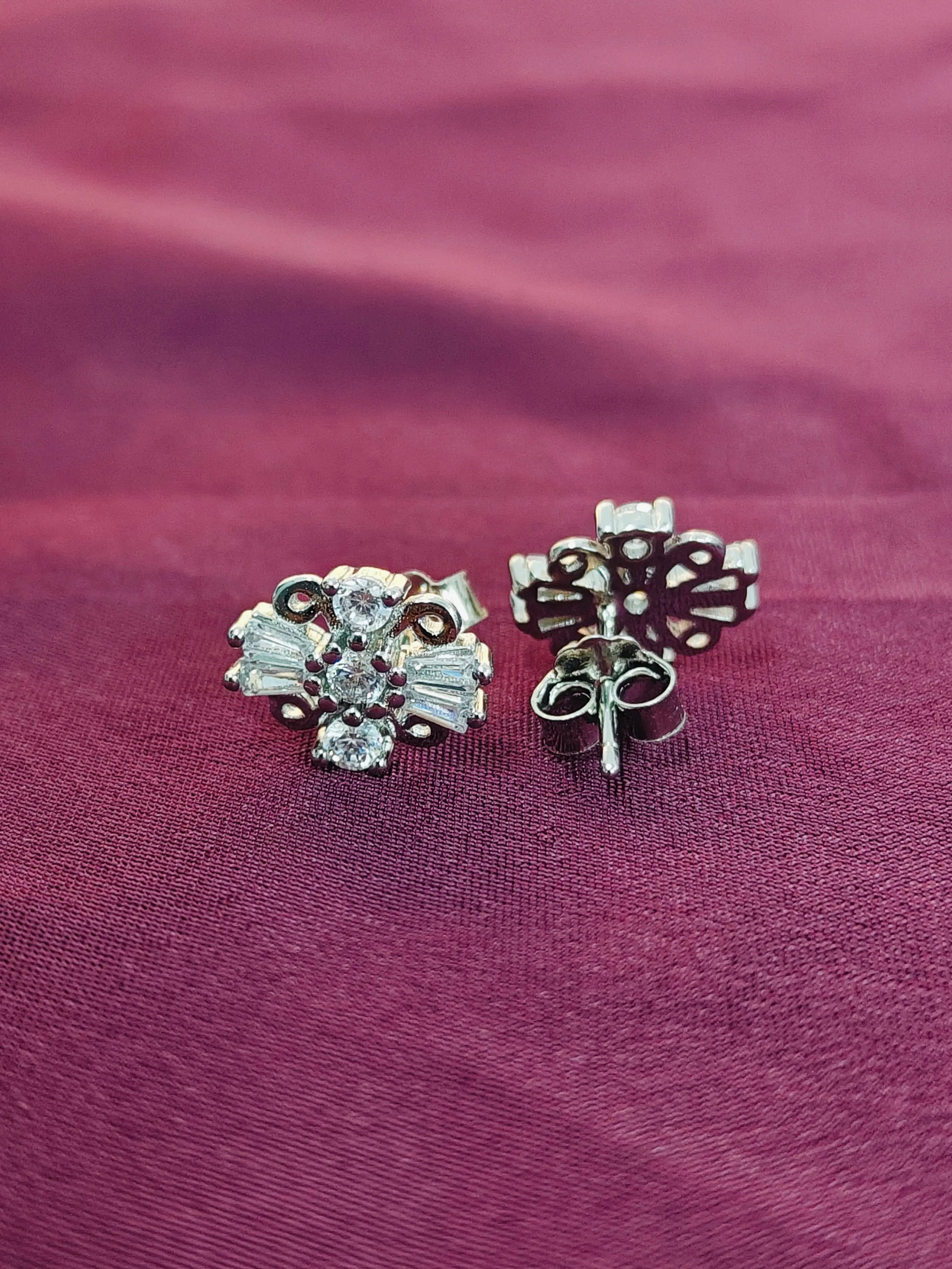 Pair of silver floral earrings on a purple fabric background