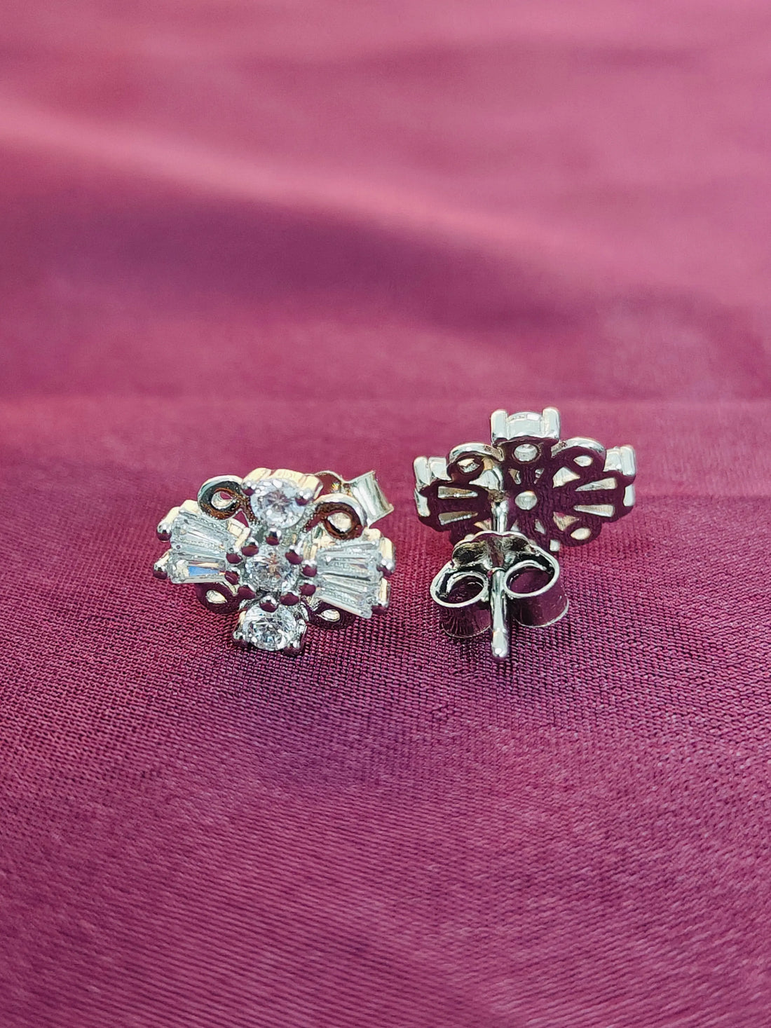 Pair of silver earrings with floral designs on a pink fabric background